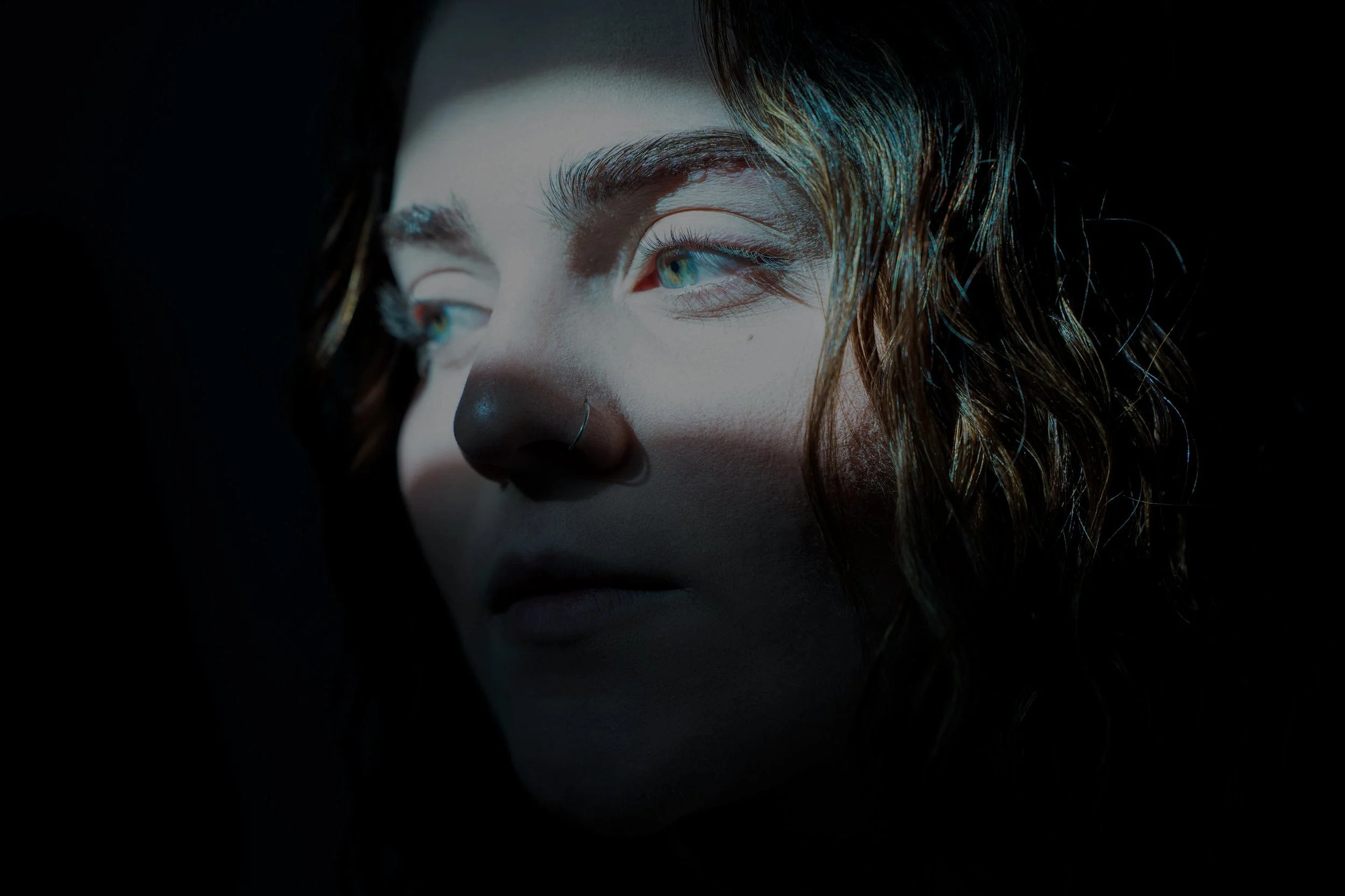 Close-up of a person's face with curly hair, looking to the side, lit from below in a dark environment.