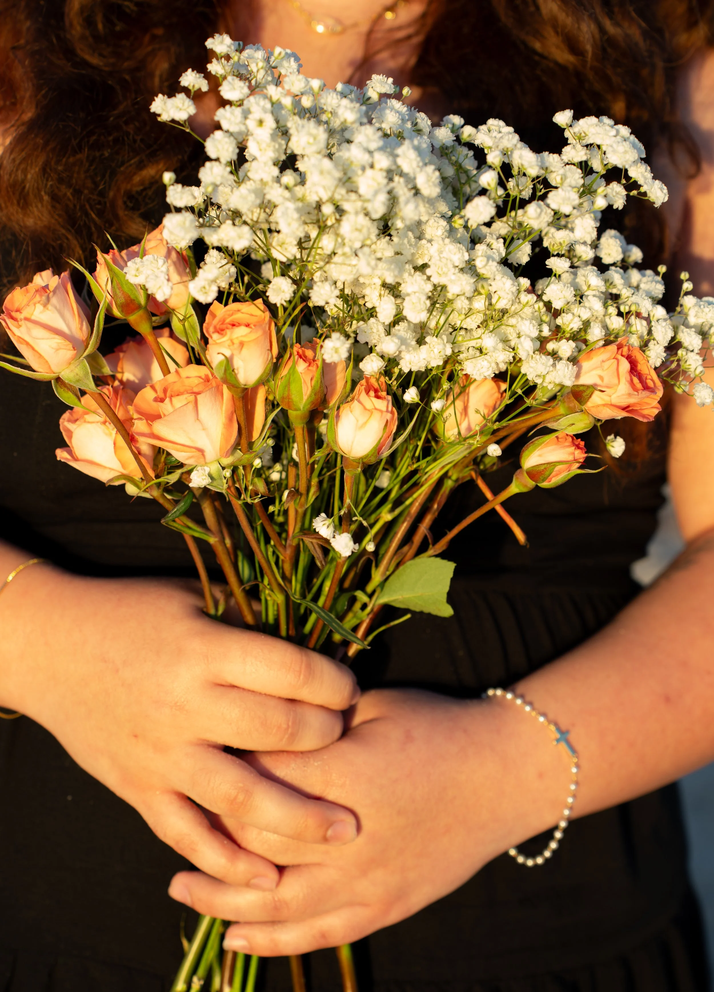 Person holding a bouquet of peach roses and white baby's breath flowers.