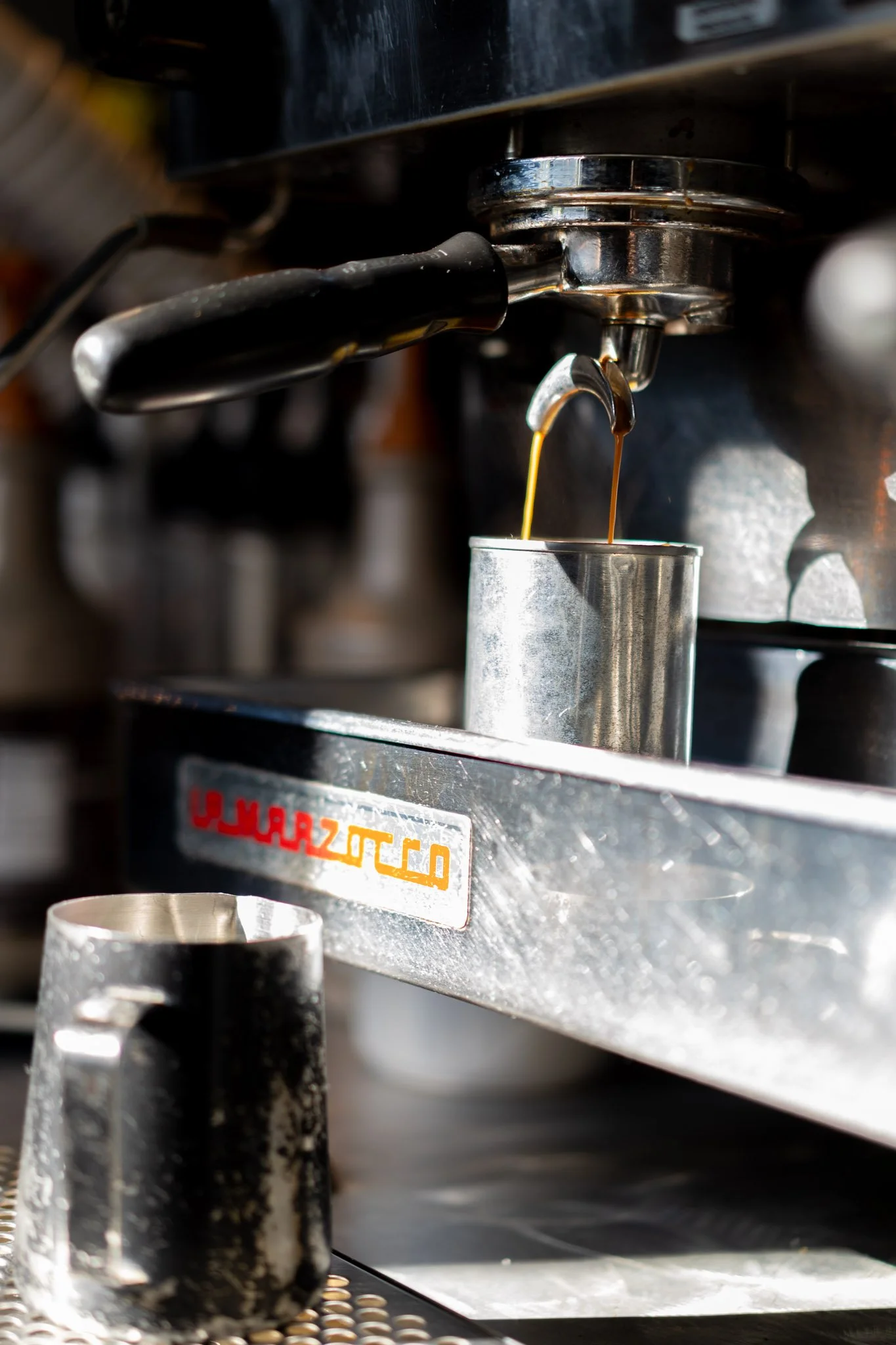 Close-up of an espresso machine pouring coffee into a metal cup, with a black mug in the foreground.