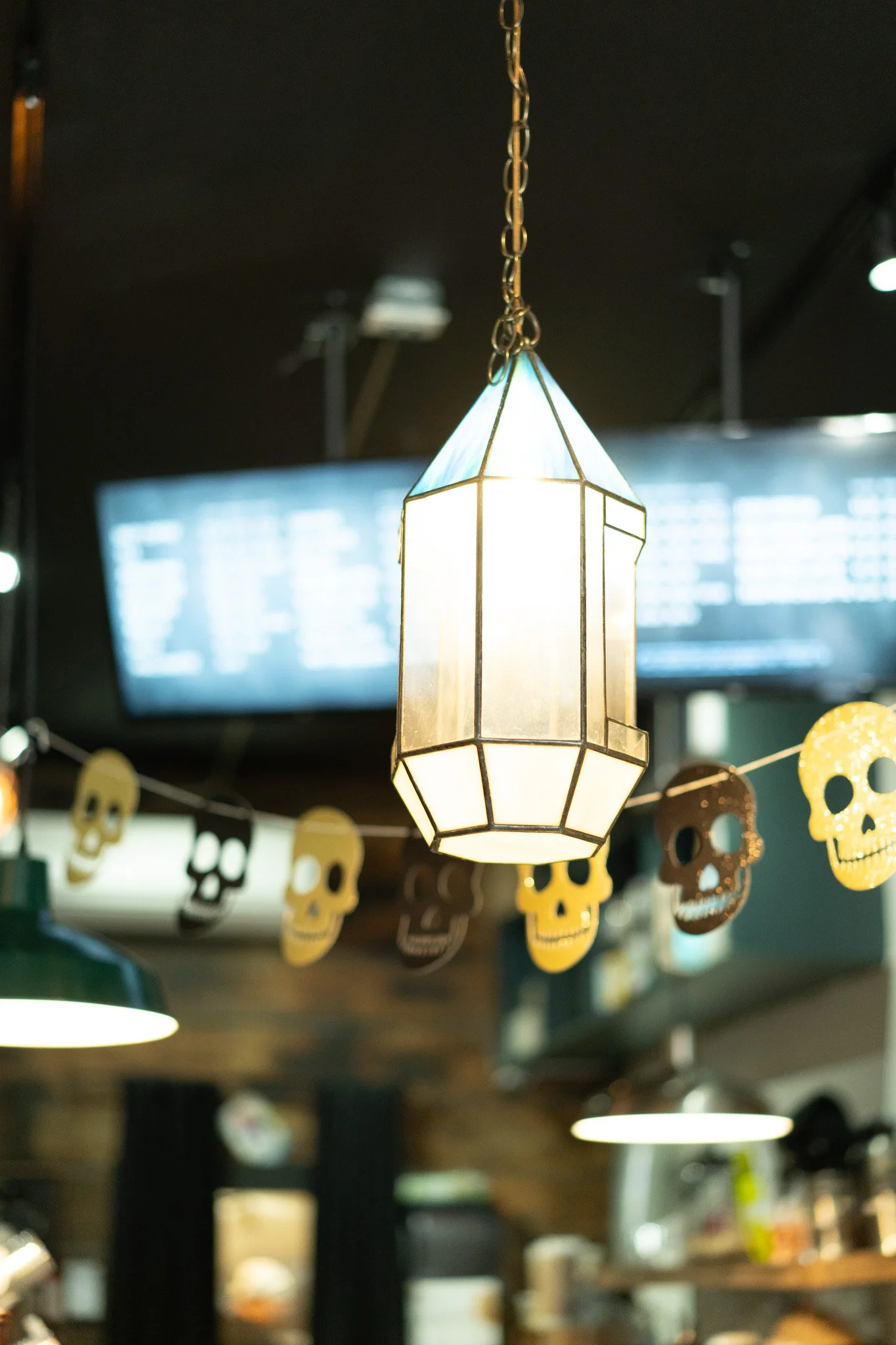 Hanging lantern light fixture in a dimly lit setting with Halloween decorations, including paper skull garlands.