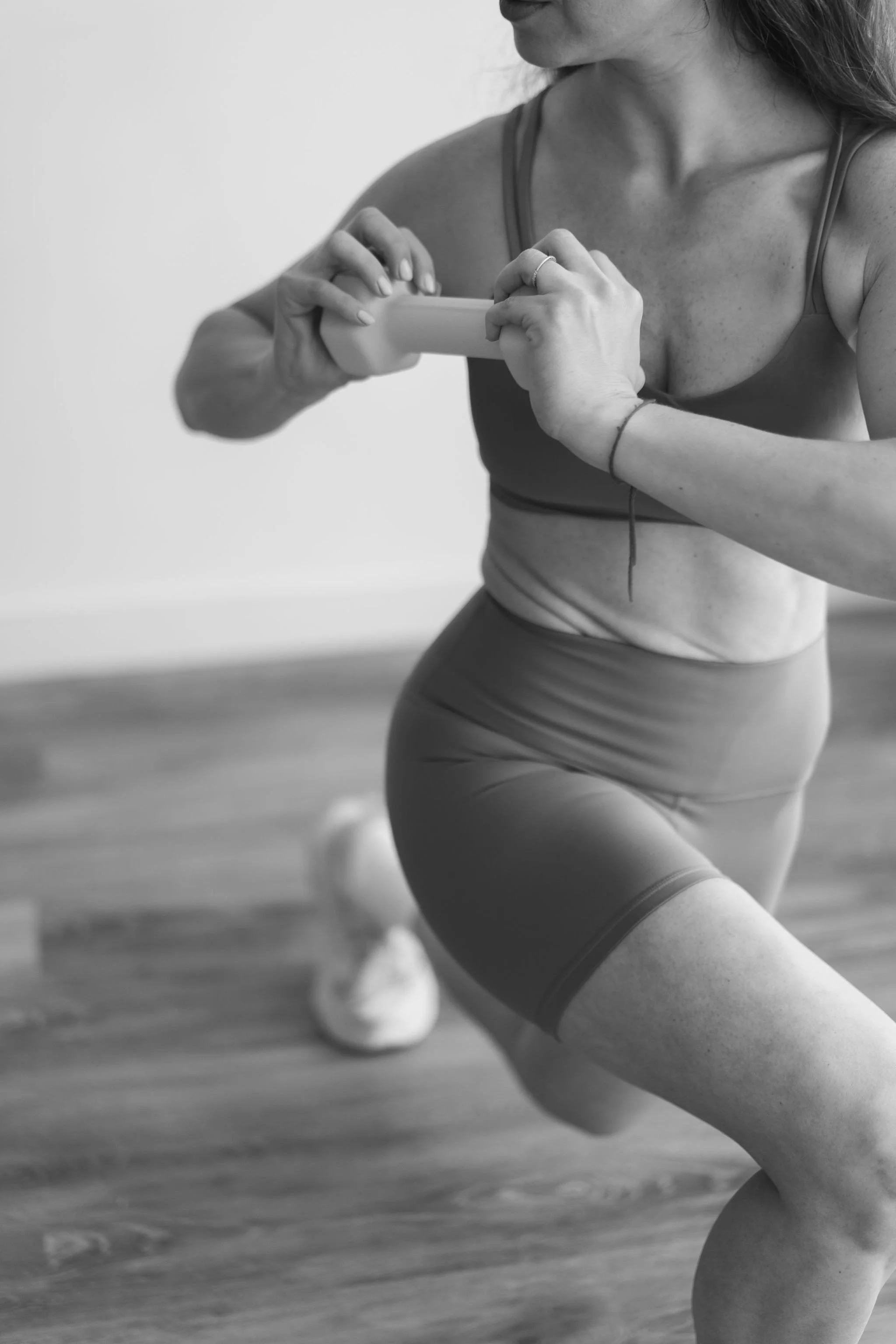 A woman in workout clothes is kneeling on the floor, taking a photo or recording with her smartphone.