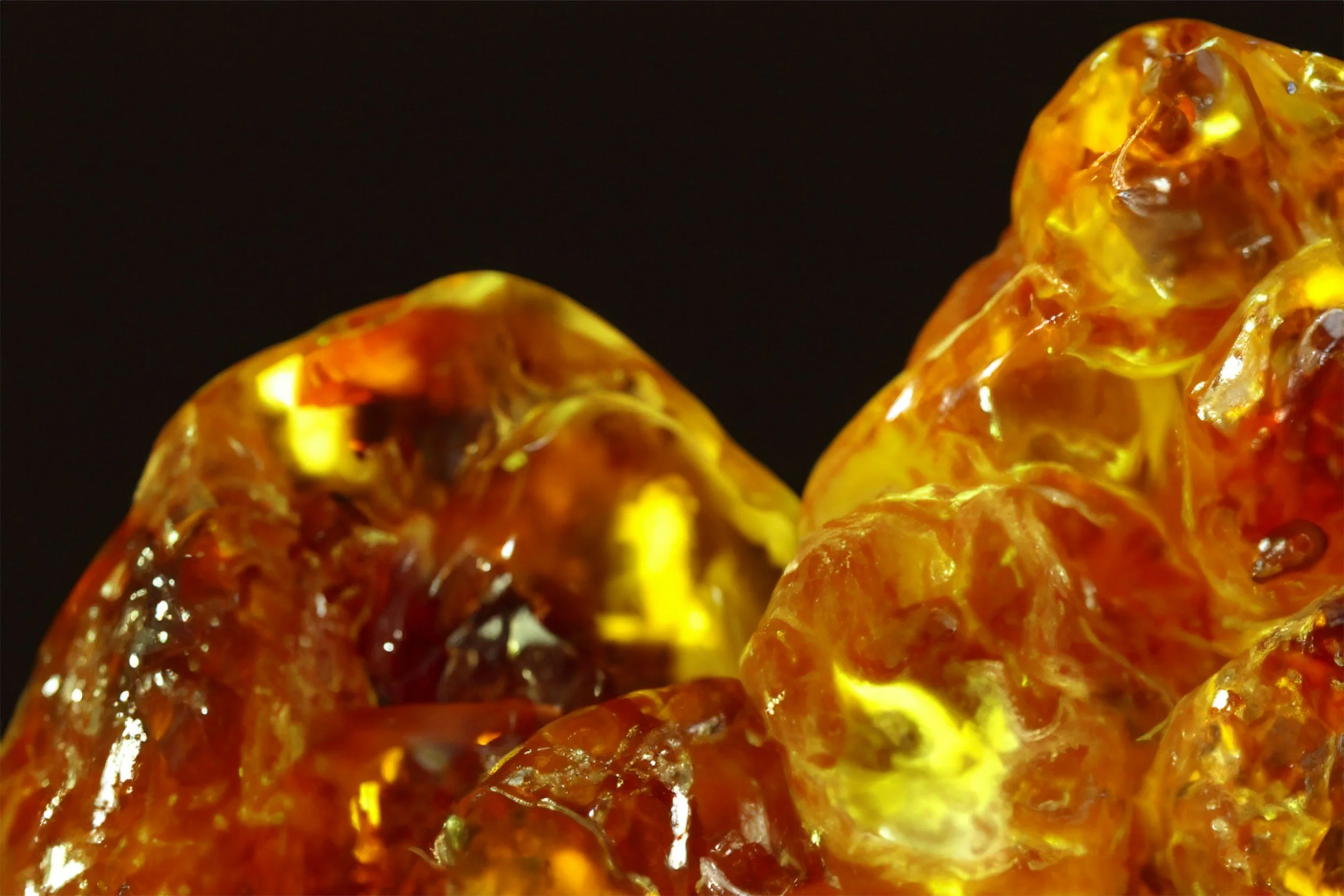 Close-up of amber-colored, translucent, irregularly shaped resin or gemstone on a black background.