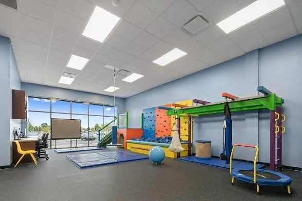 Kids play area with climbing wall, trampoline, balloon, and sports equipment in a brightly lit room with blue walls and large window