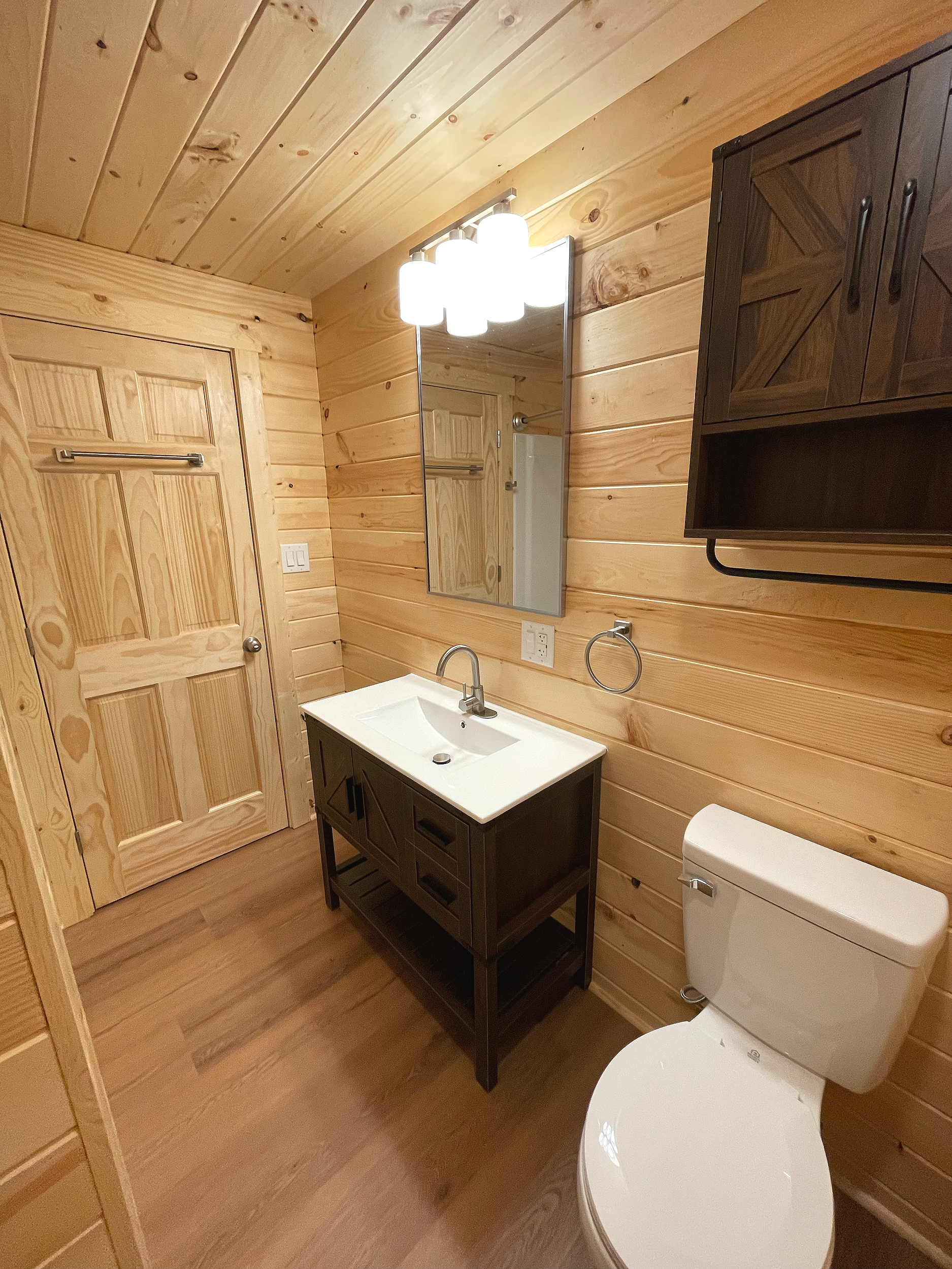 Wood-paneled bathroom with a white sink, mirror, wooden cabinets, and a toilet.