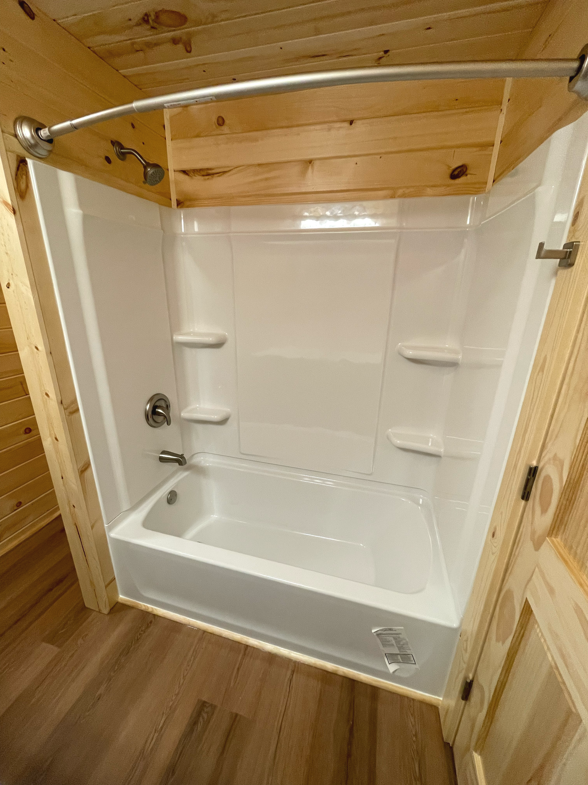 A walk-in shower with a wooden wall and ceiling, white tiled walls, a handheld showerhead, and a built-in shower seat.
