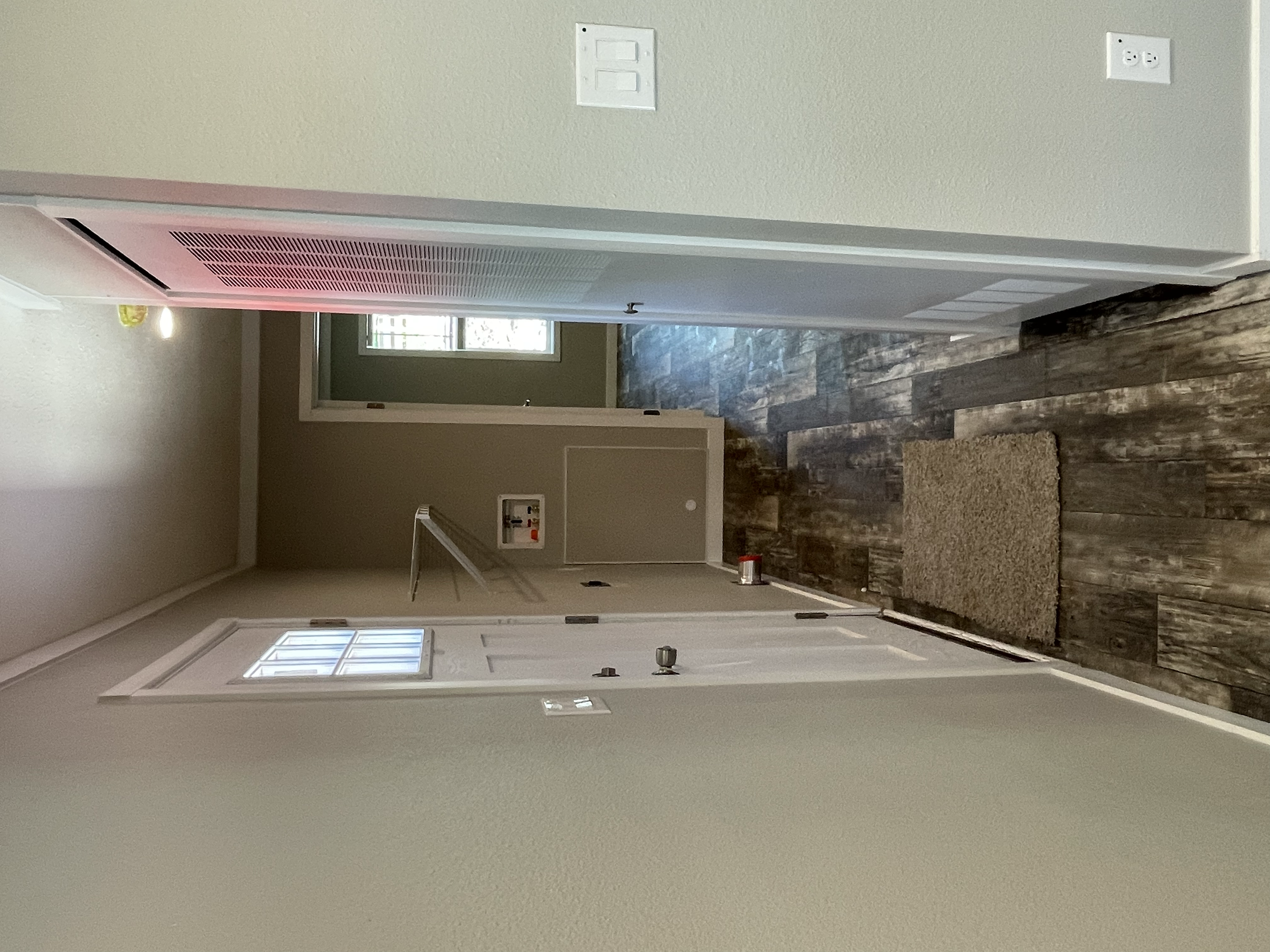 Empty hallway with wood-look vinyl flooring, beige walls, and a white ceiling. There are two windows at the end of the hallway letting in natural light. A small fire alarm box is mounted on the wall near the ceiling, and an electrical outlet is visib