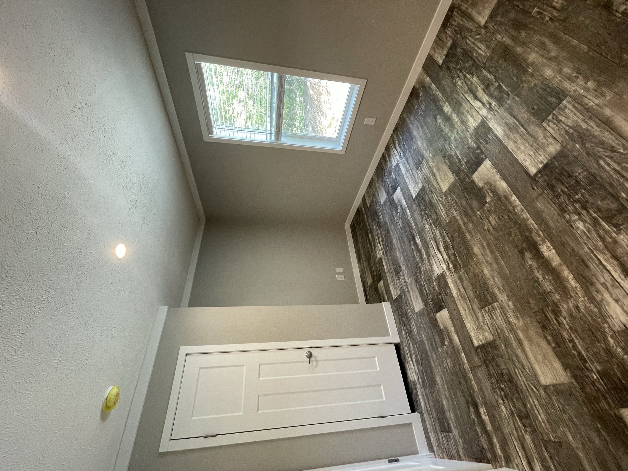Empty room with a window, white door, textured white wall, dark wood flooring, and an overhead light.