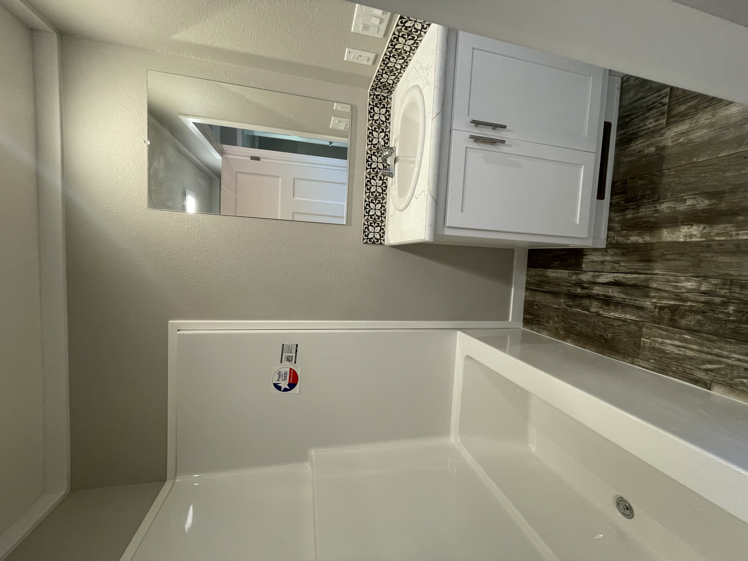 A bathroom vanity area with a mirror, a sink, and a white cabinet, with decorative black and white tile accents on the countertop, and wood-like flooring.
