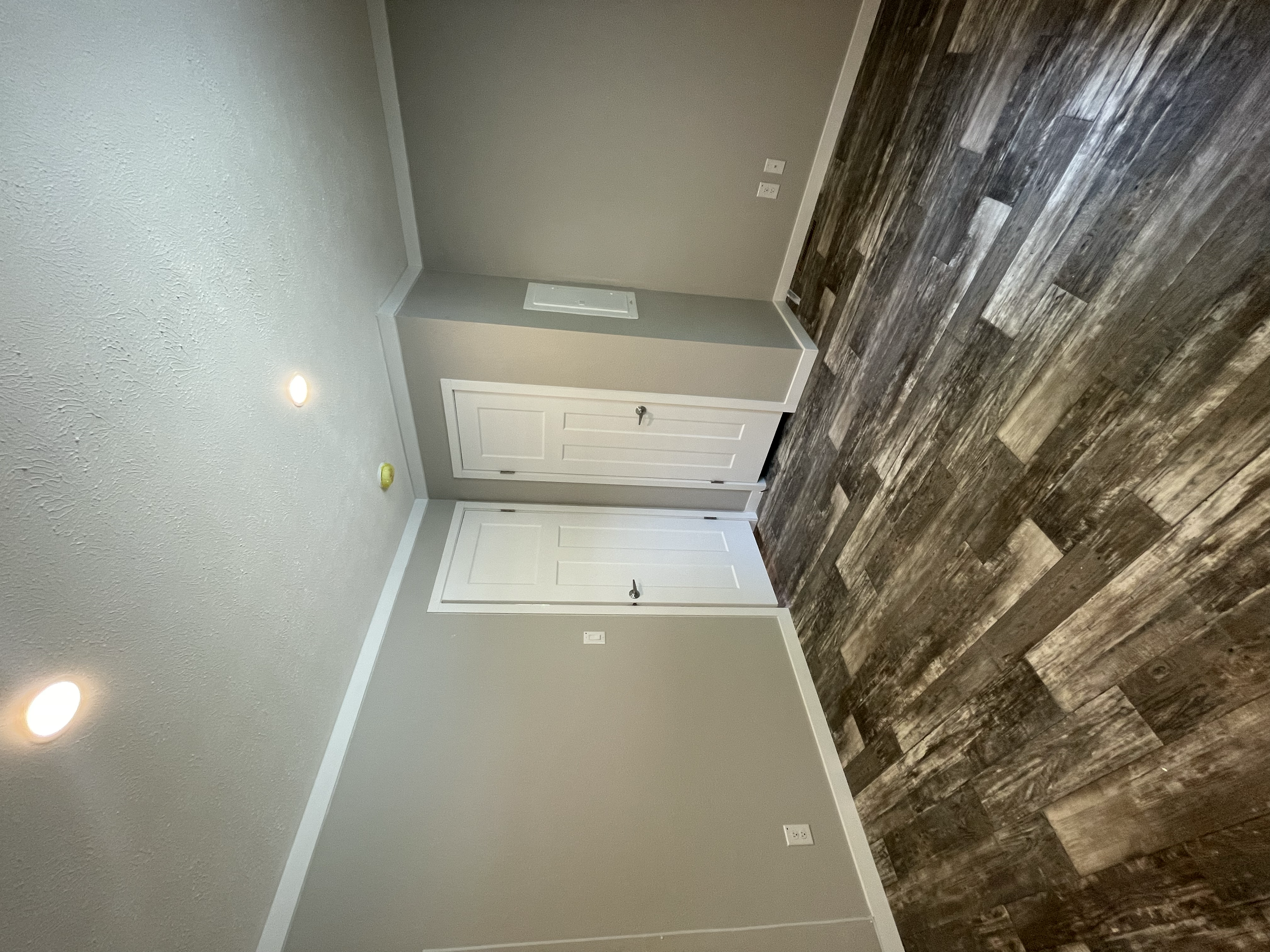 Empty room with hardwood floor, light gray walls, white baseboards, white door, and electrical outlets.