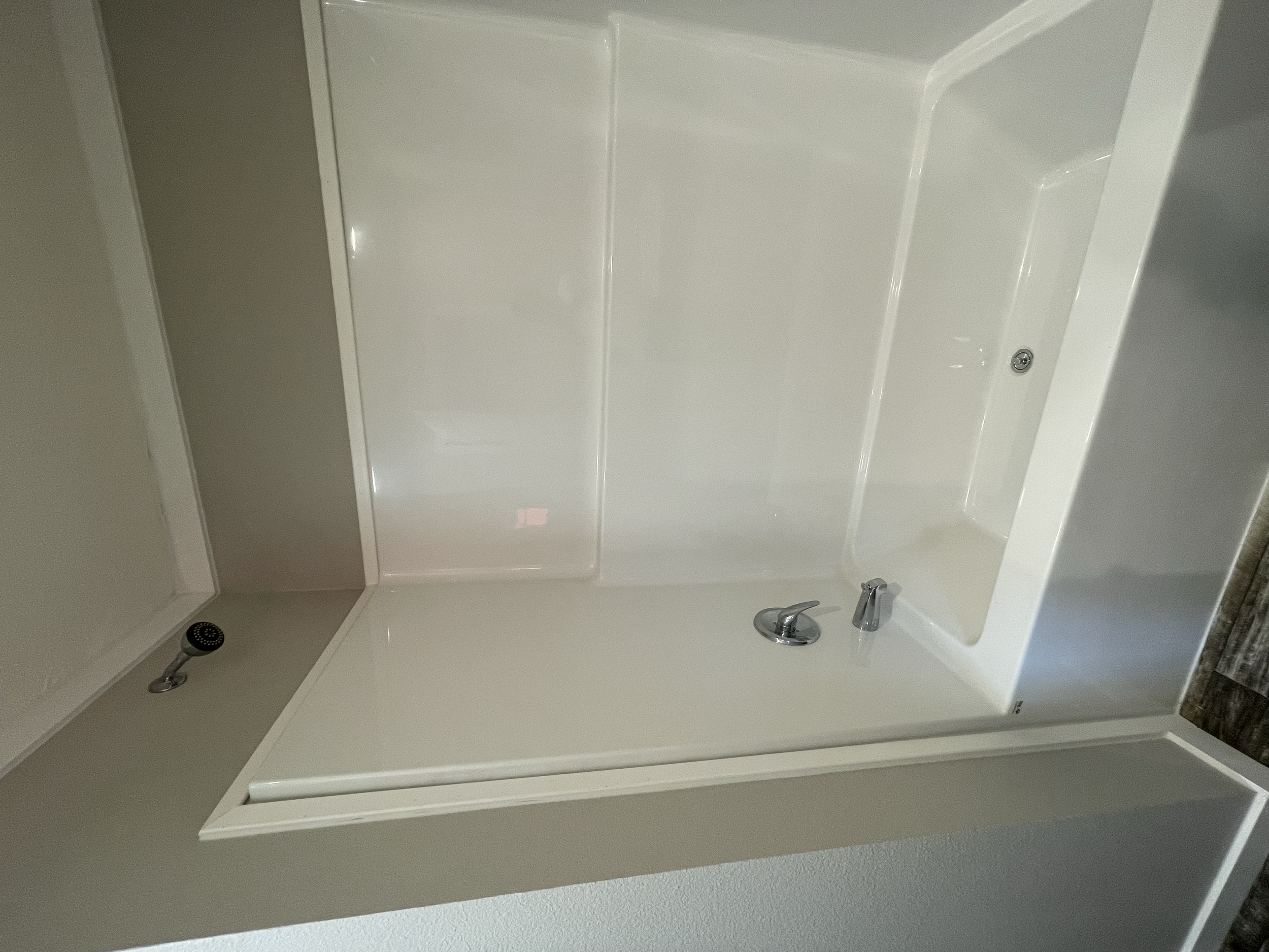 A bathroom shower with a glass door, a handheld showerhead, and a small soap dish on the wall.