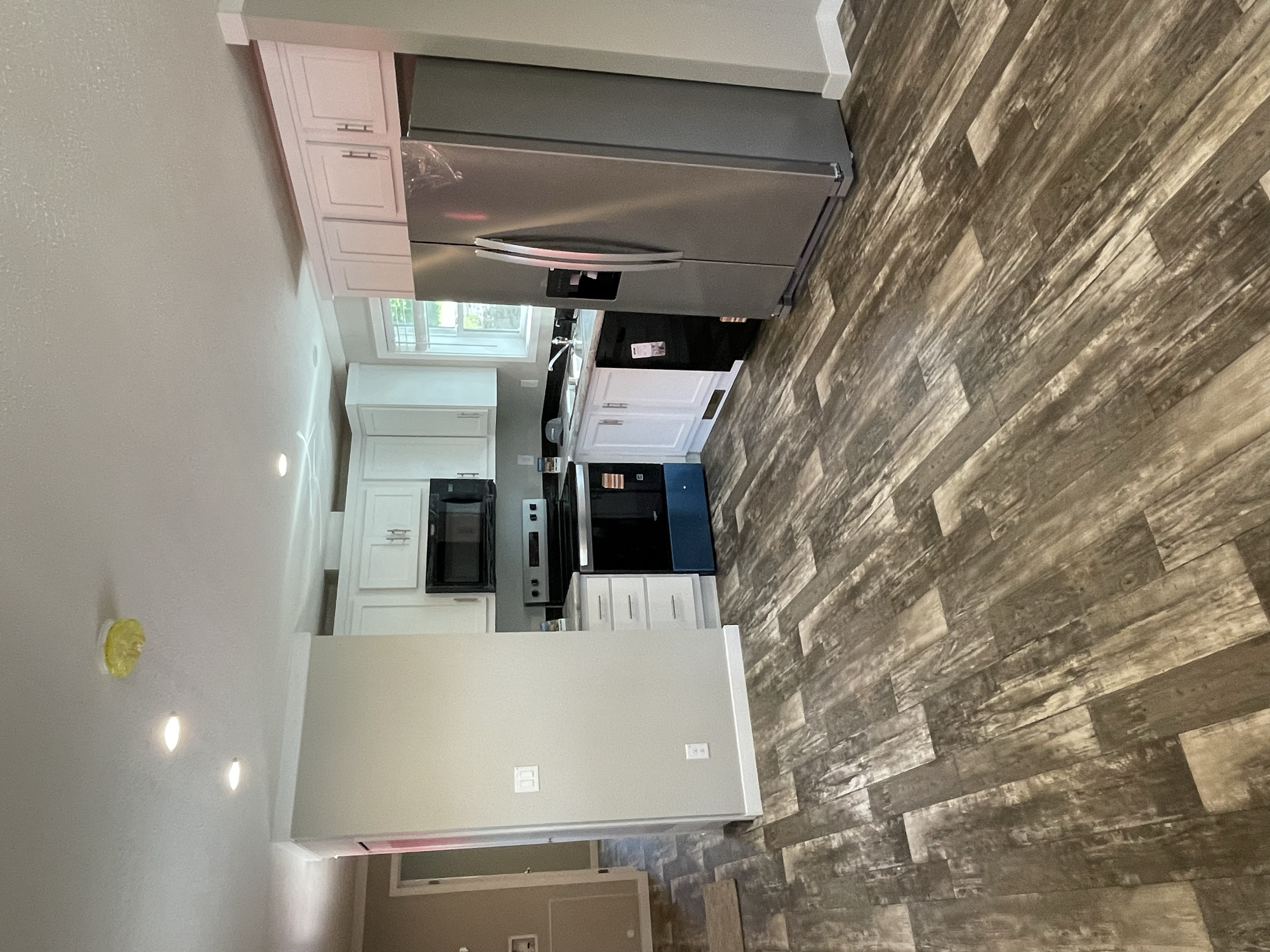 Kitchen with white cabinets, stainless steel refrigerator, black oven, and wood-look flooring.