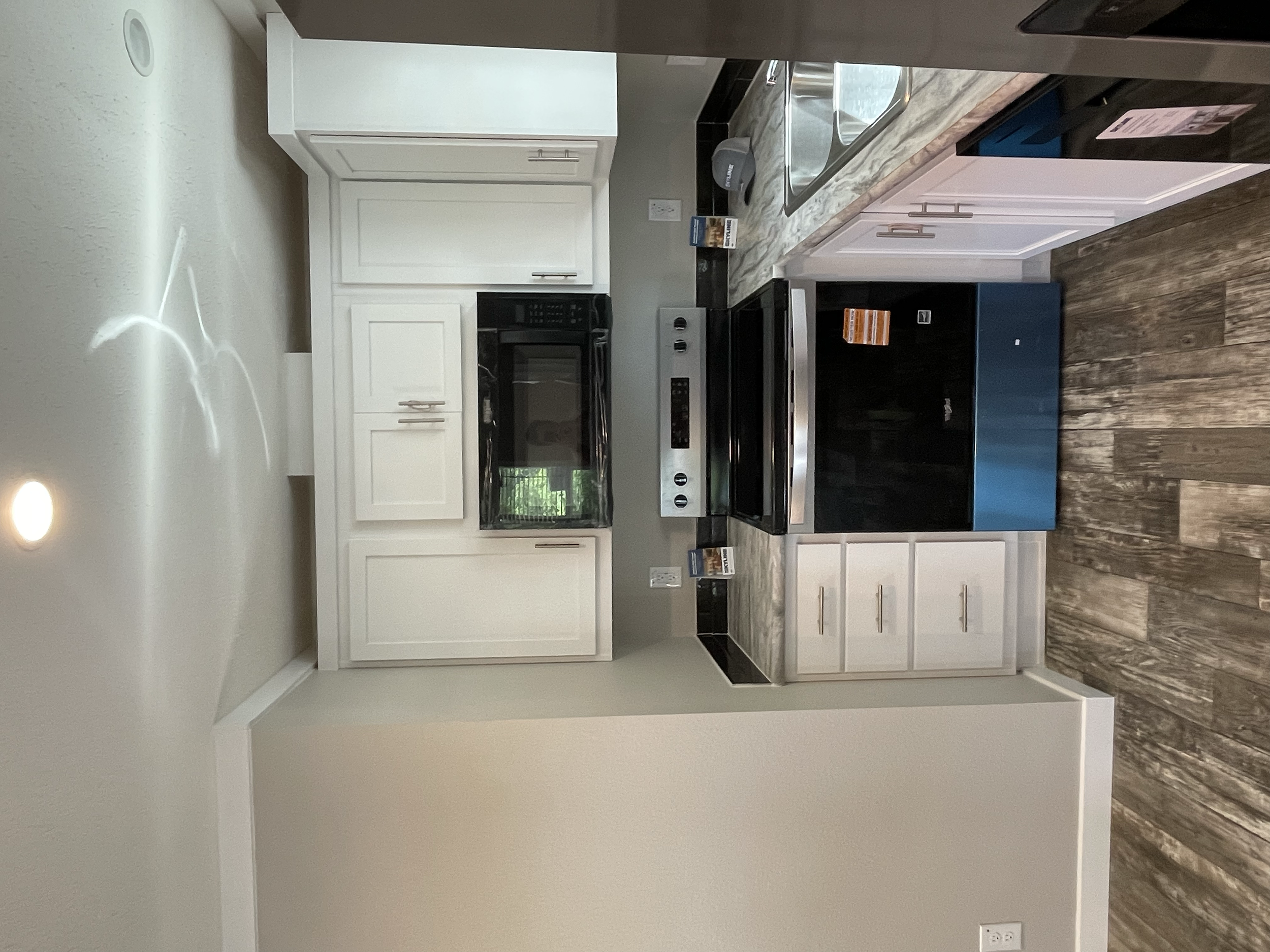 View of a kitchen with white cabinets, black appliances, a marble countertop, a stainless steel sink, wood flooring, and a small blue cabinet.