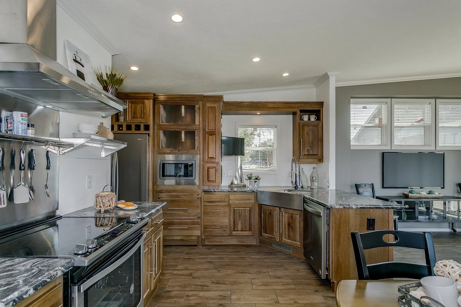 Modern kitchen with wooden cabinets, stainless steel appliances, granite countertops, a window, and a dining area with a black chair.