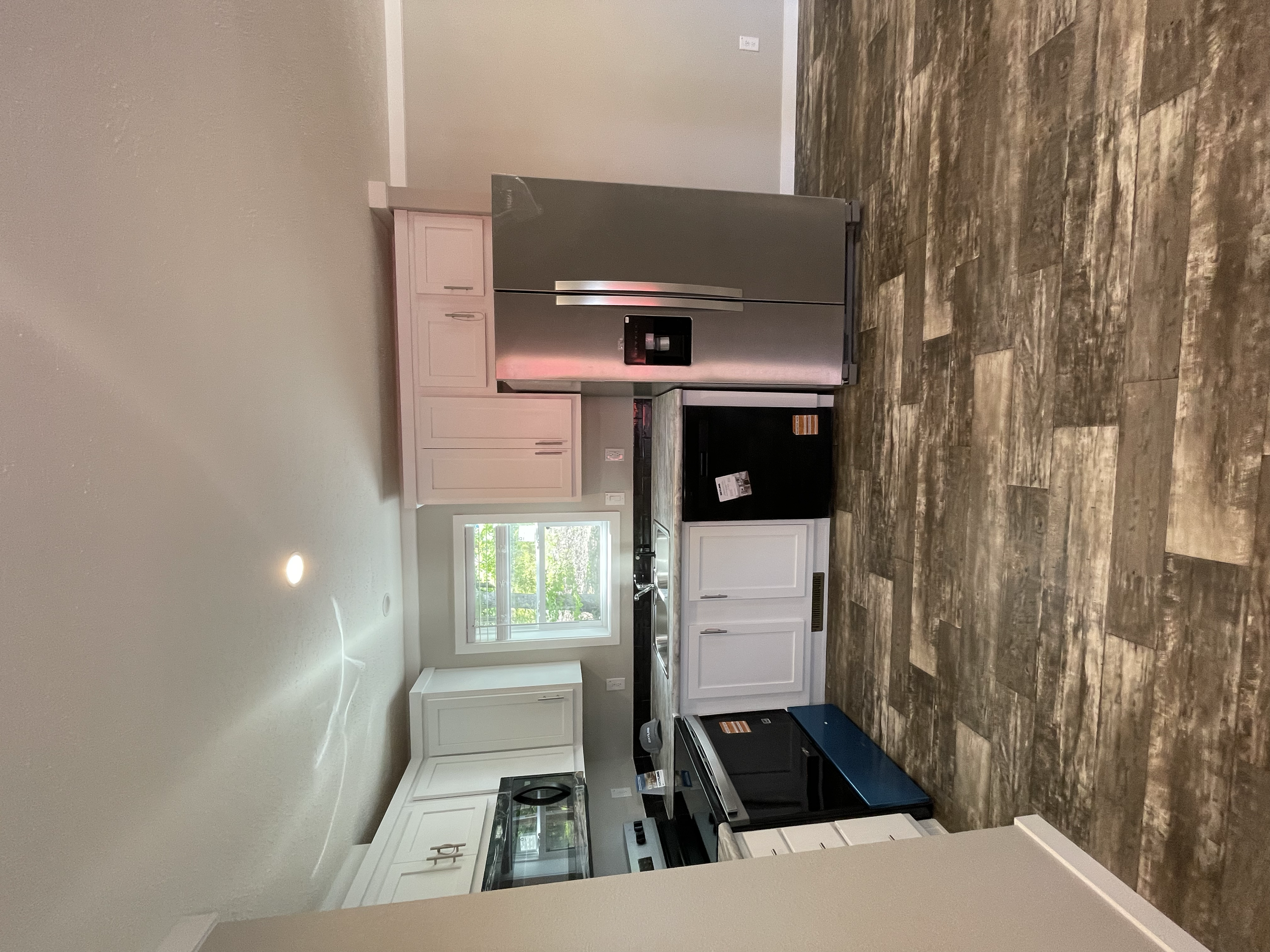 Modern kitchen with white cabinets, black appliances, stainless steel refrigerator with water and ice dispenser, wood-look tile flooring, and a window above the sink
