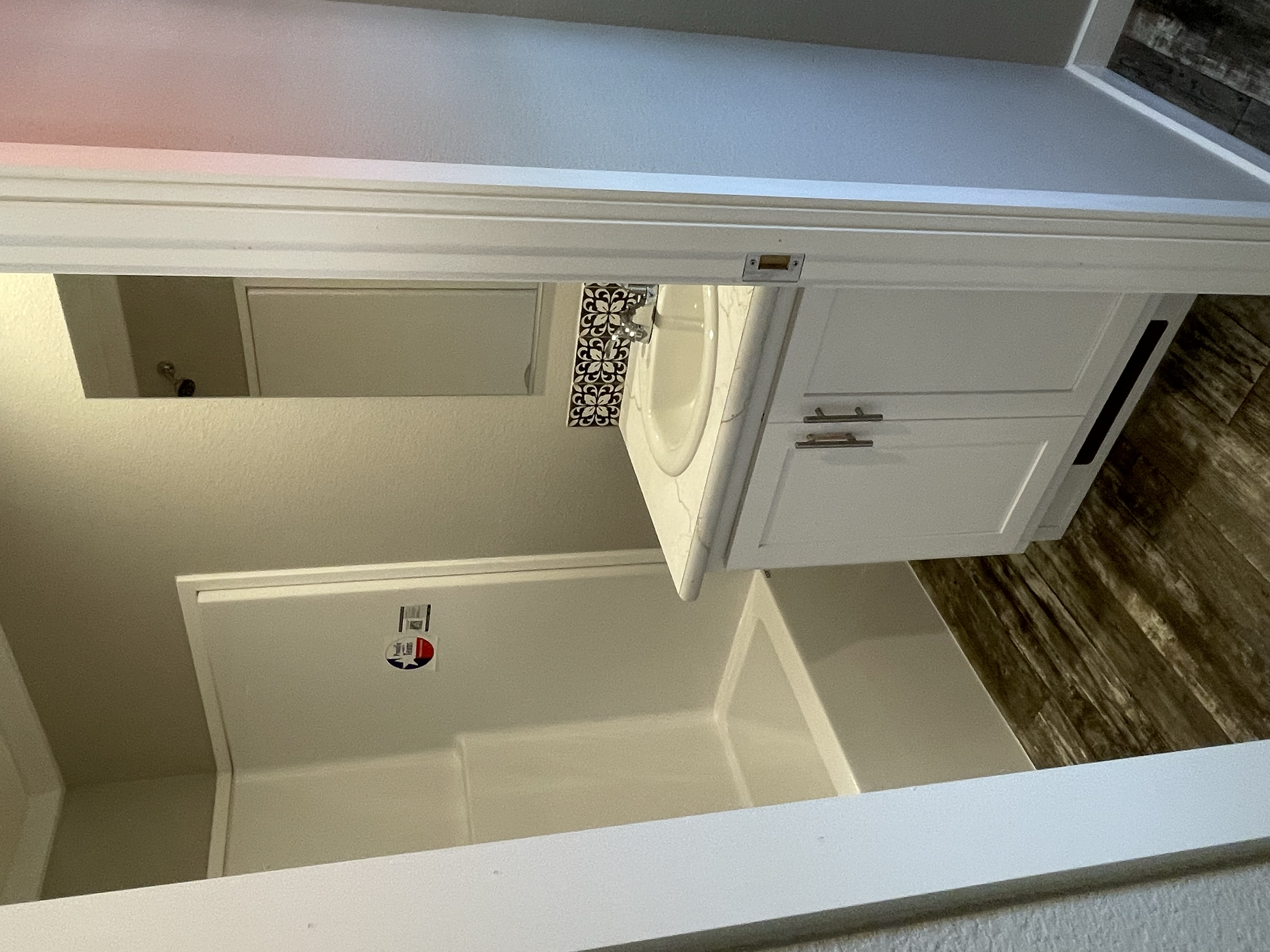 View of a bathroom bathroom with a white vanity, sink, and decorative tile behind the sink, a mirror, and an open doorway revealing a hallway.