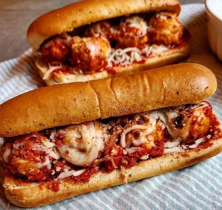 Two meatball sub sandwiches with melted cheese on a bun, served on a striped paper liner.