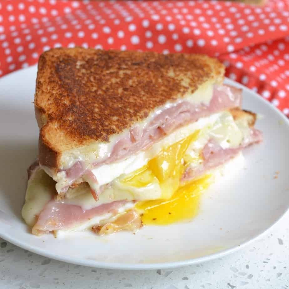 Close-up of a breakfast sandwich with fried egg, ham, and melted cheese between two slices of toasted bread.