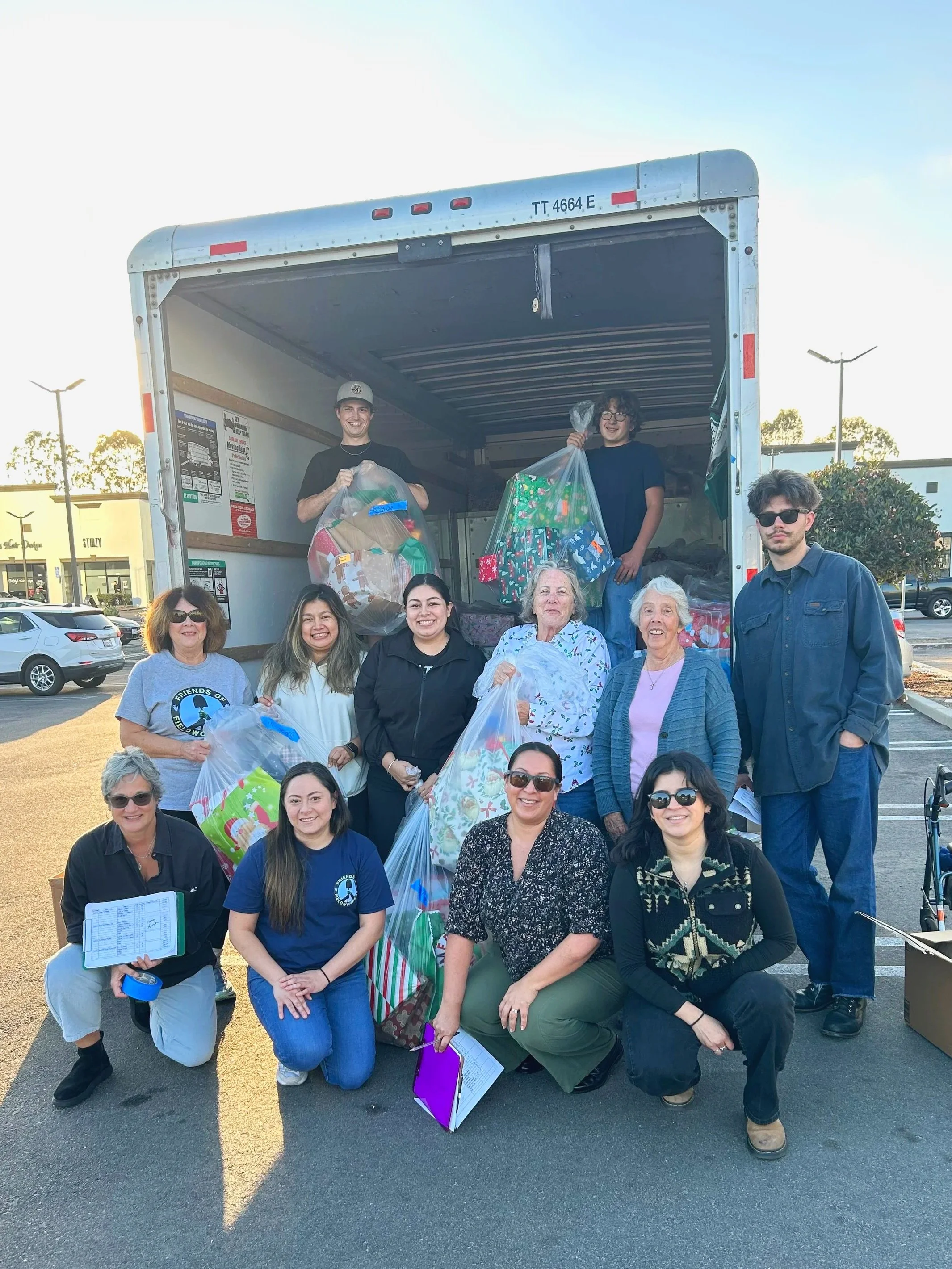 Group of volunteers with bags of holiday toys in a parking lot, smiling for a photo.
