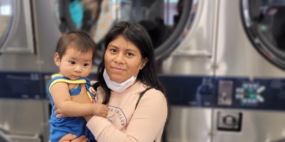 A woman holding a young child in front of laundry machines in a laundromat