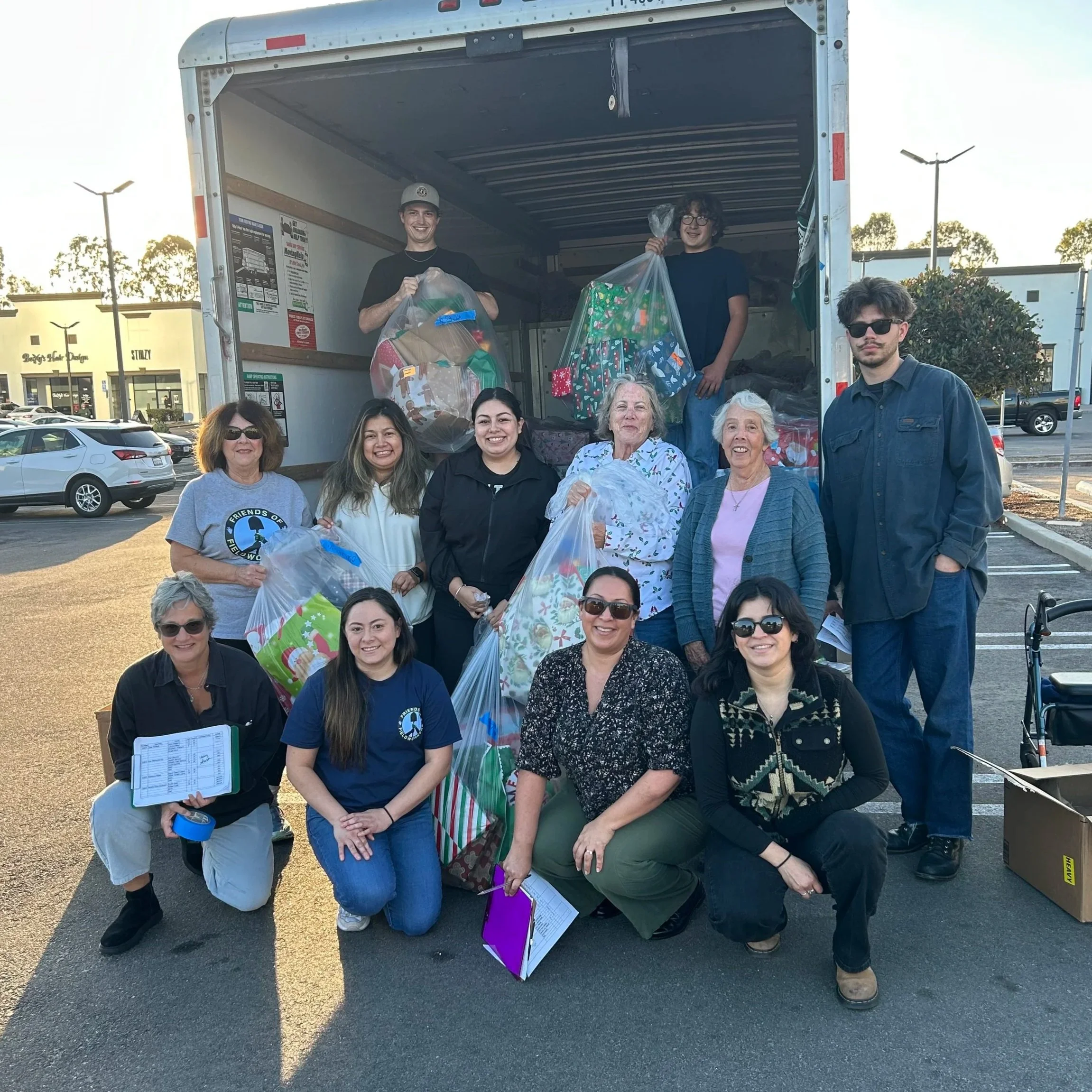 Group of volunteers carrying donations and bags outside a truck in a parking lot during daytime.