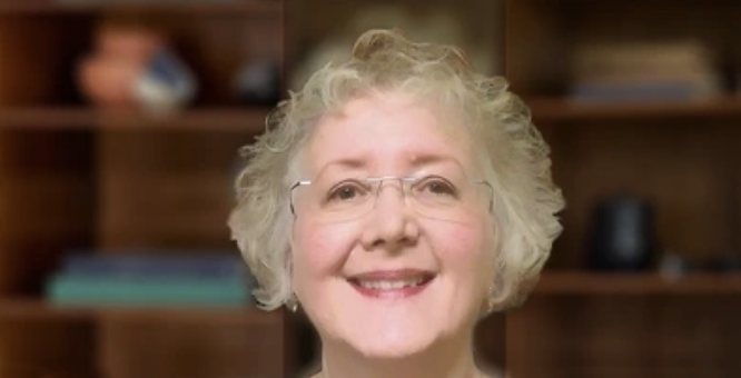 Smiling elderly woman with glasses in a room with wooden shelves and books.