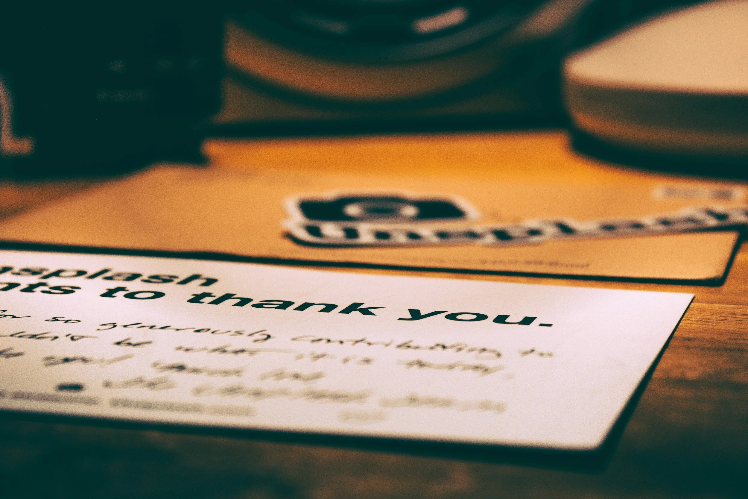 Close-up photo of a handwritten note on paper with a thank you message, with a blurred orange and black background.