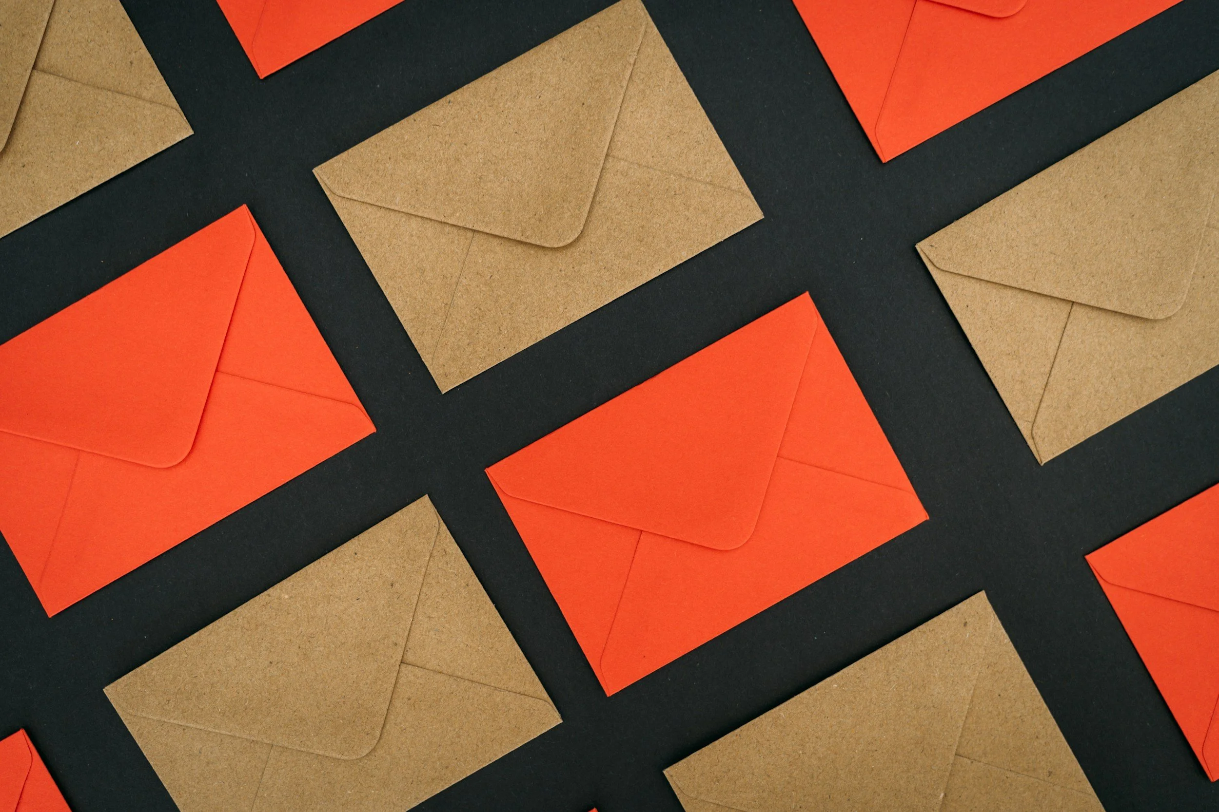 Multiple kraft paper and orange envelopes arranged on a dark surface.