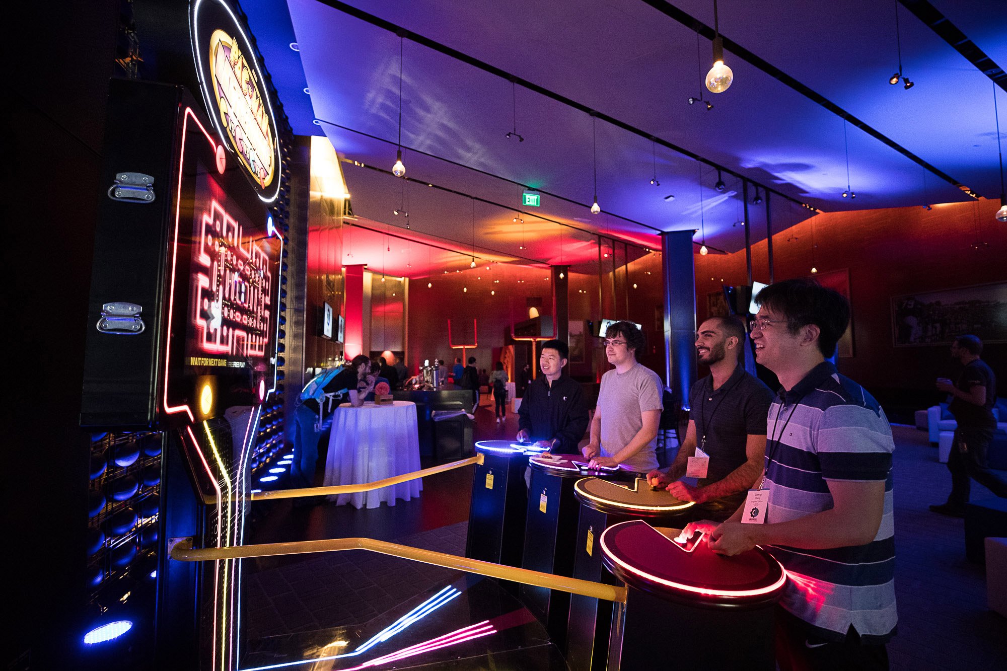 People playing an arcade game with neon lights in a dimly lit entertainment venue.
