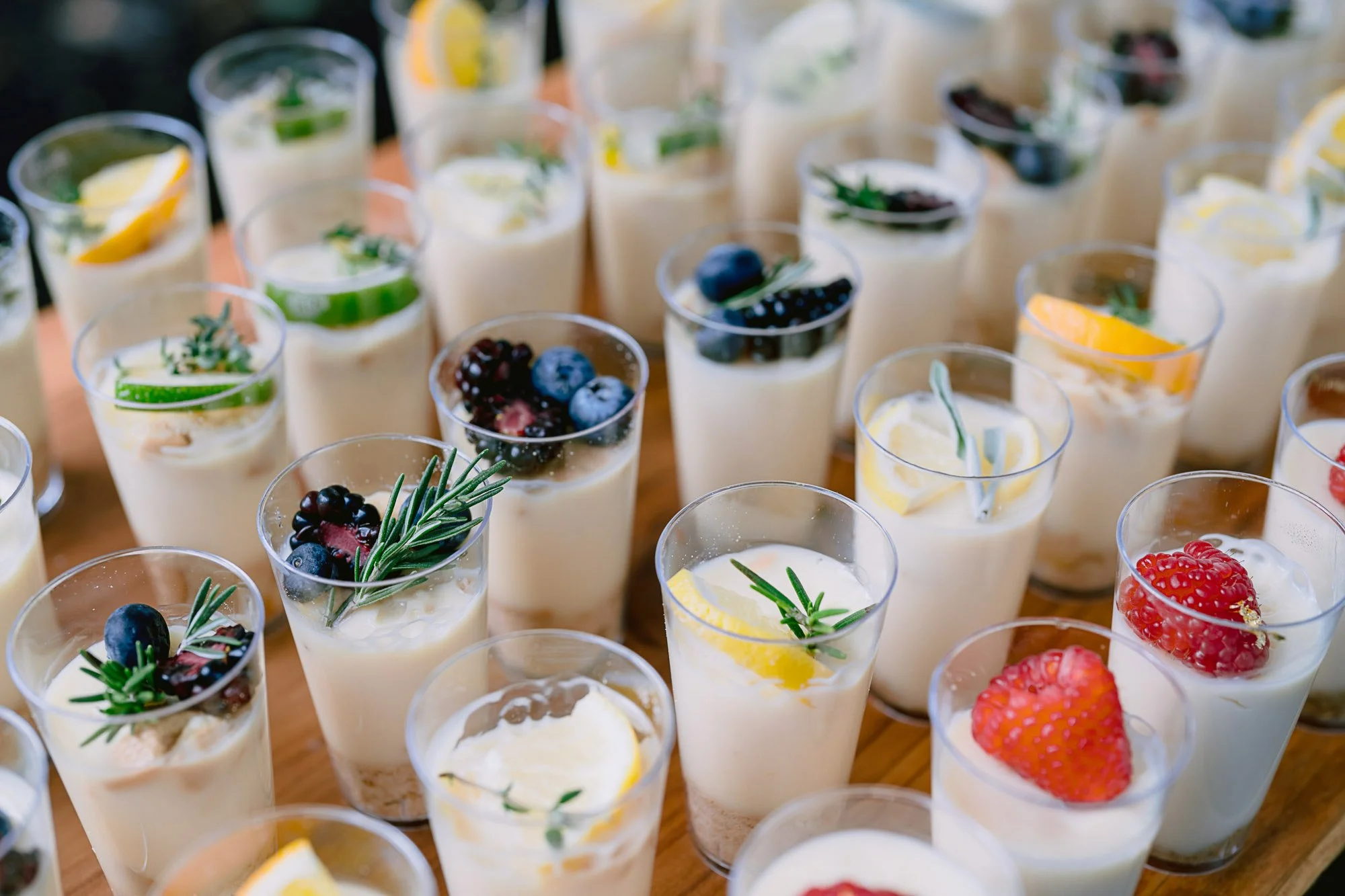 Several small glasses filled with creamy dessert topped with fresh berries and lemon slices.