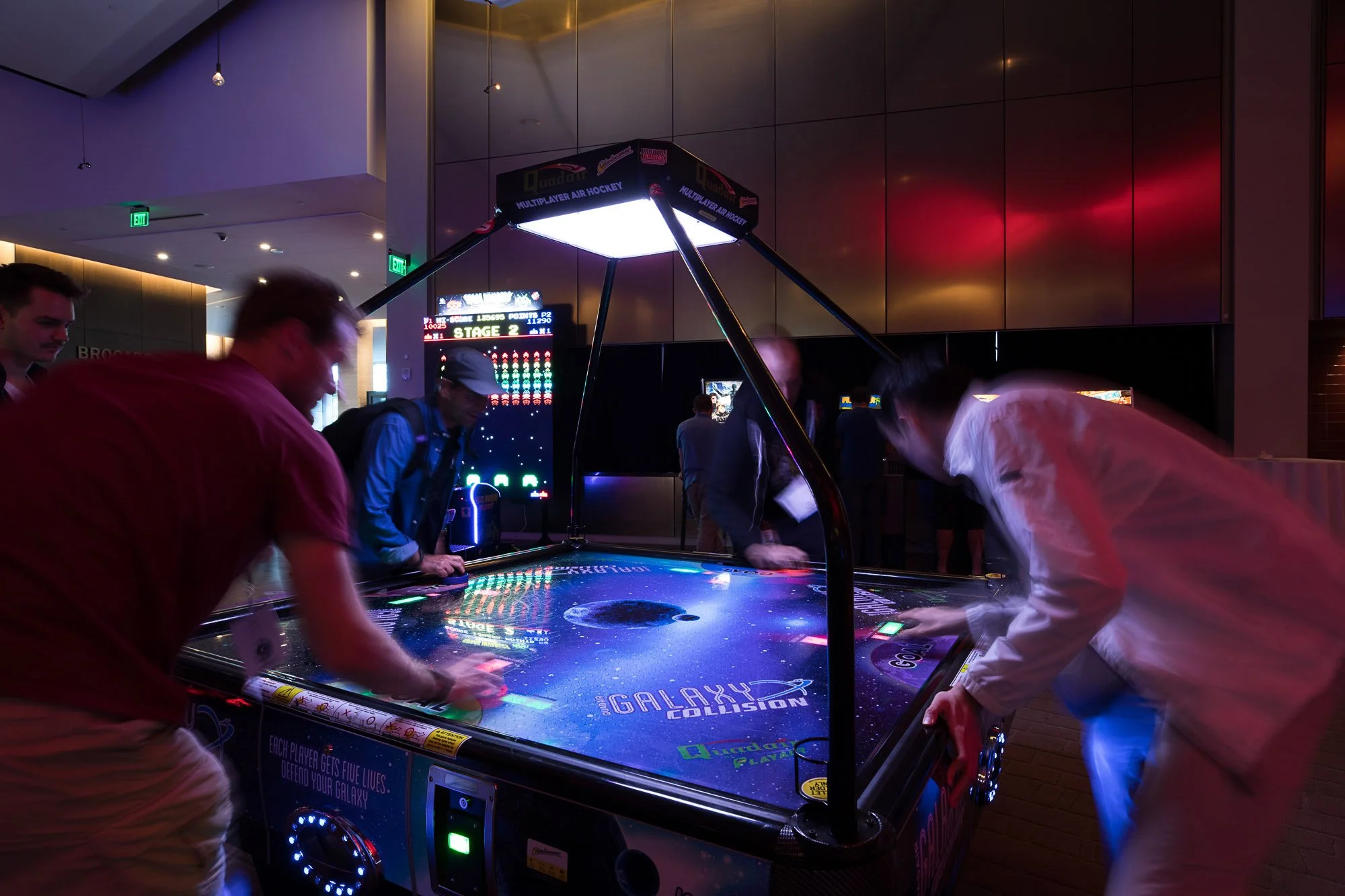 People playing Galaxy Collision arcade game in a dimly lit arcade area with electronic screens and lighting.