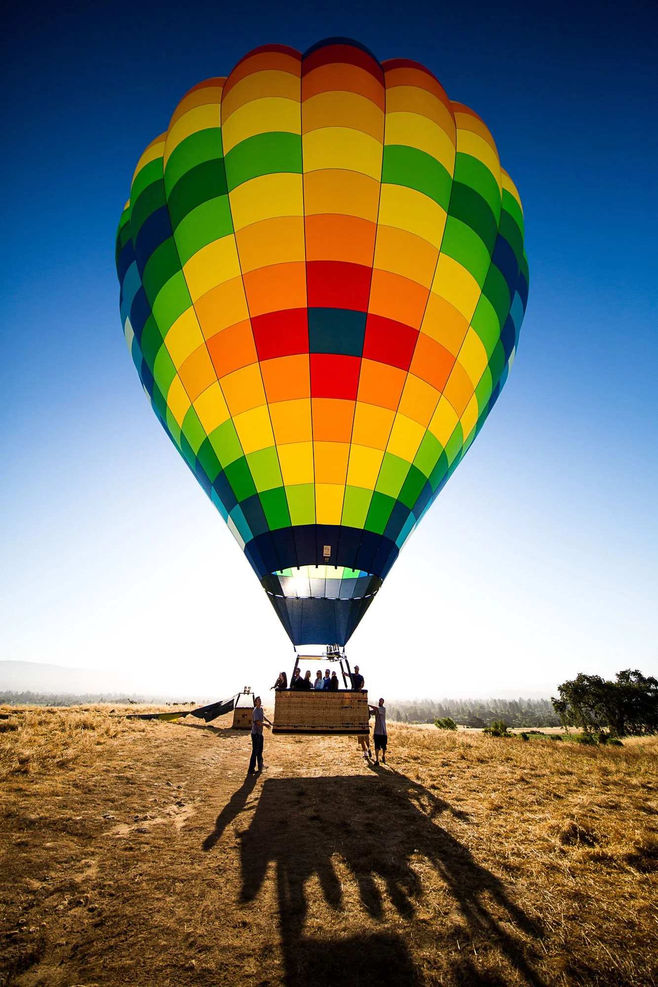 Colorful hot air balloon with rainbow stripes being prepared for flight on a grassy field at sunrise.
