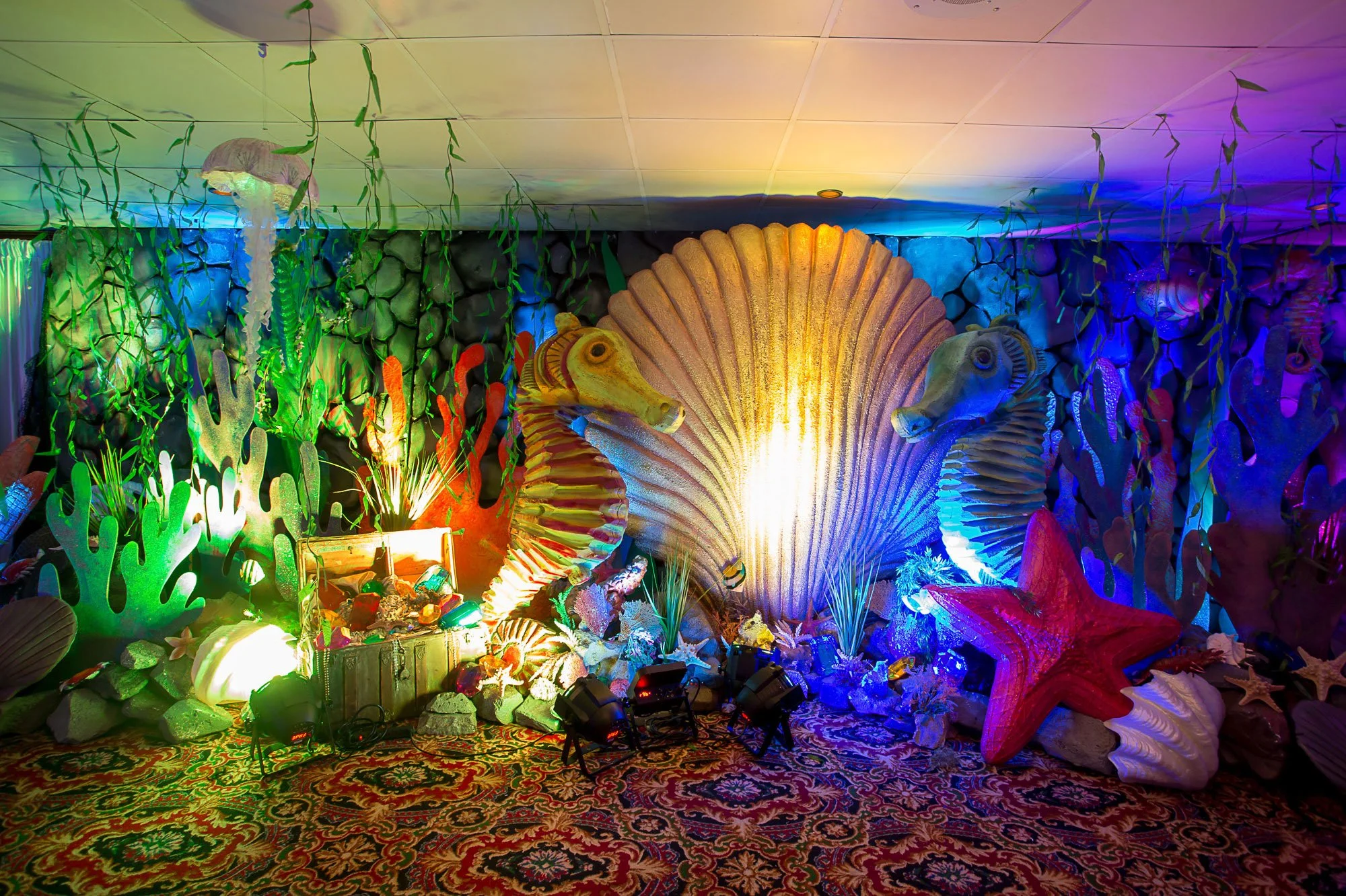 Colorful underwater or ocean-themed decorations, including large seashells, coral, seaweed, and sea creature sculptures, illuminated with vibrant lighting.