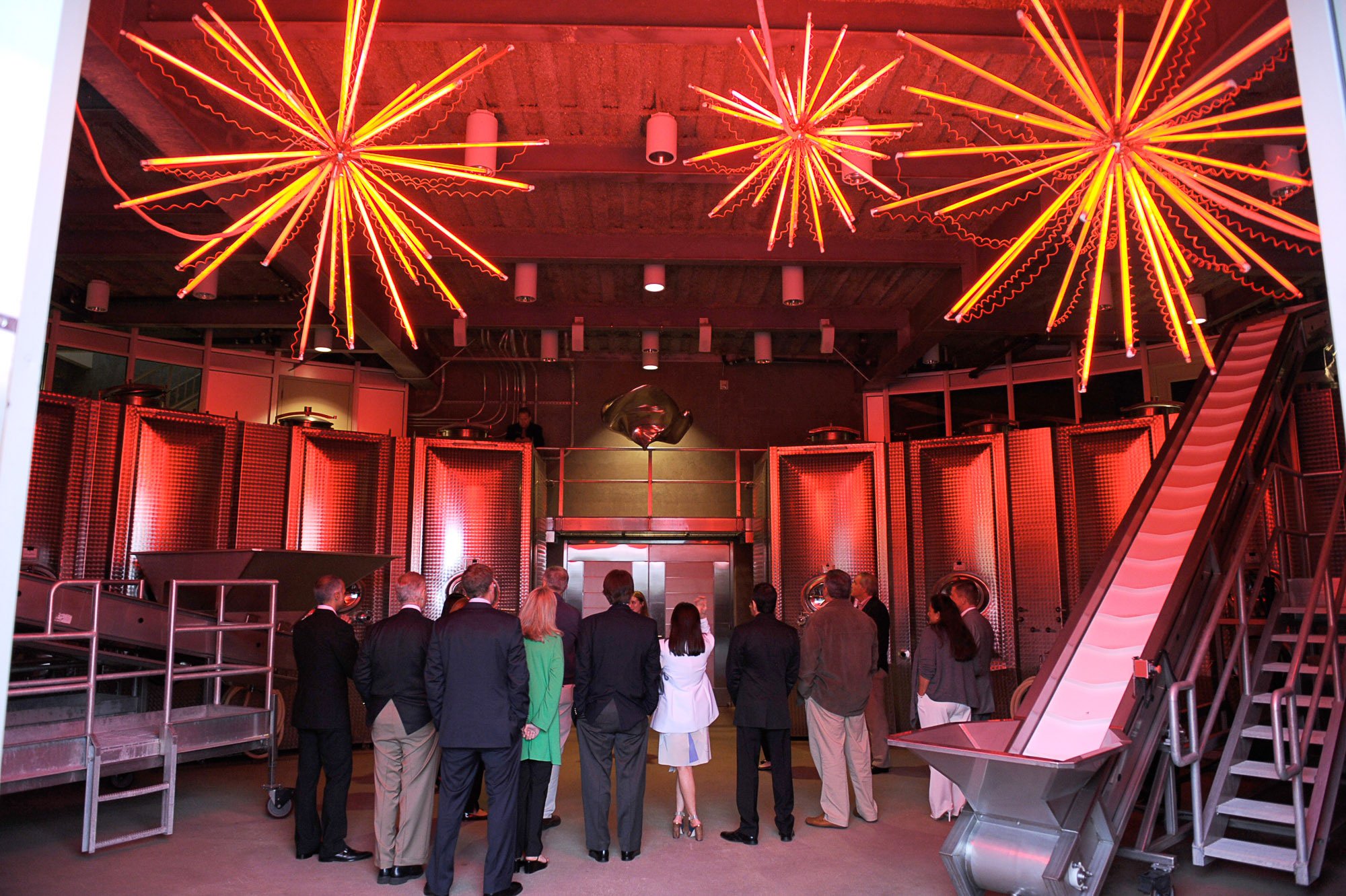 People dressed in formal attire attending an event in an industrial-style venue with bright red neon light fixtures hanging from the ceiling.