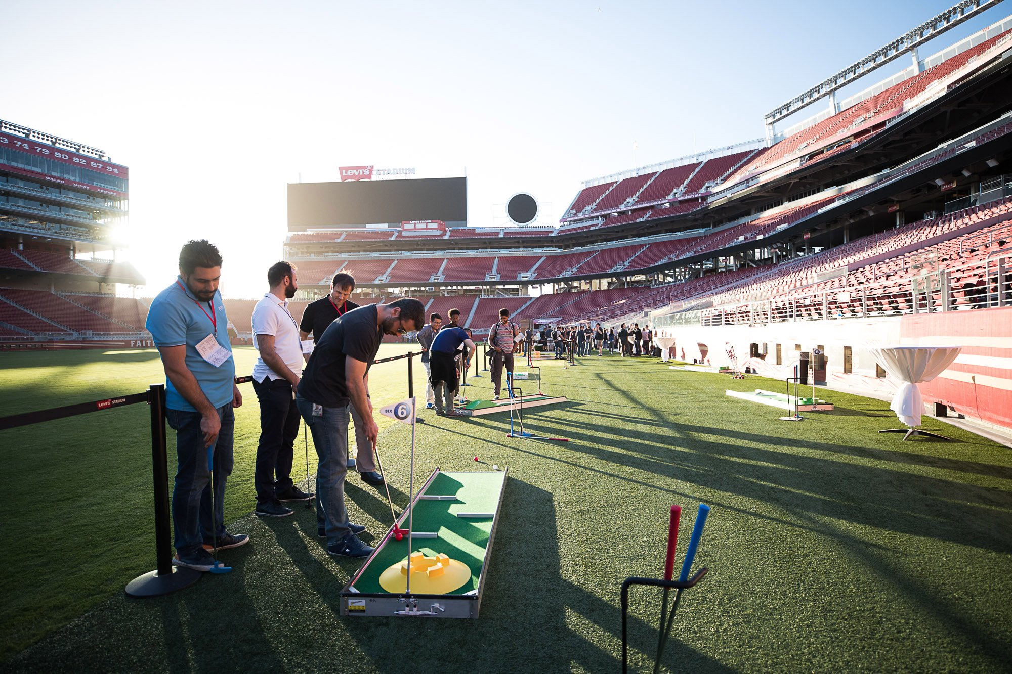 People gathered at Levi's Stadium practicing miniature golf on a synthetic grass field during a sunny day.