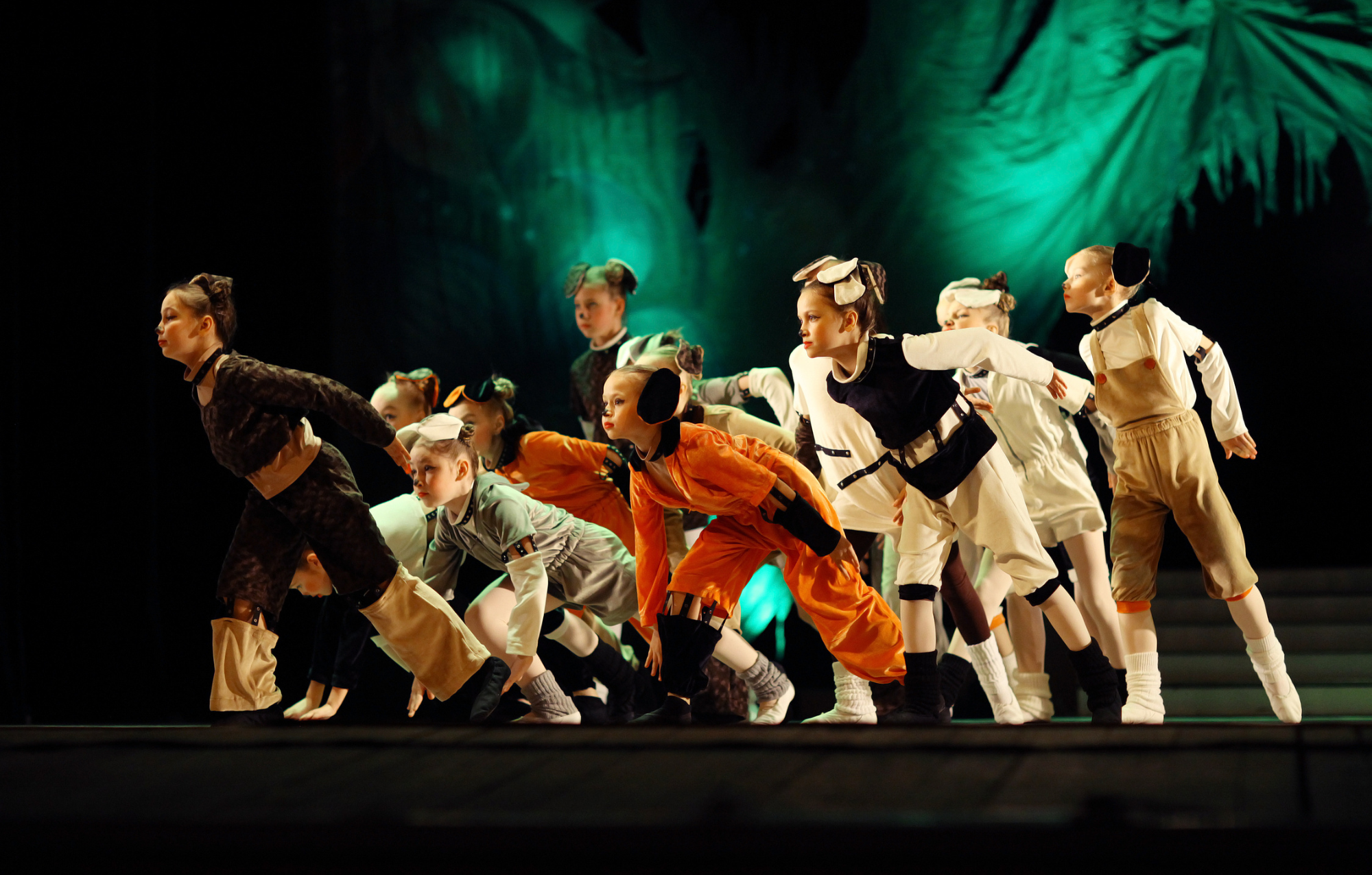 Children in animal costumes performing on stage during a dance recital with green stage lighting and a dark backdrop.