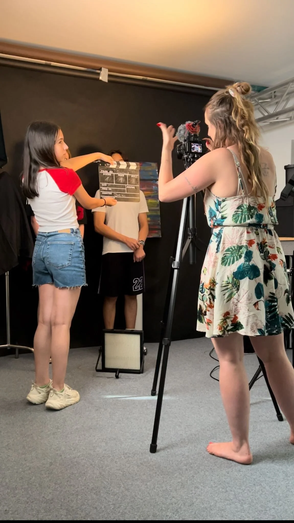 A girl with a clapperboard filming a scene with a director and crew members in a studio.