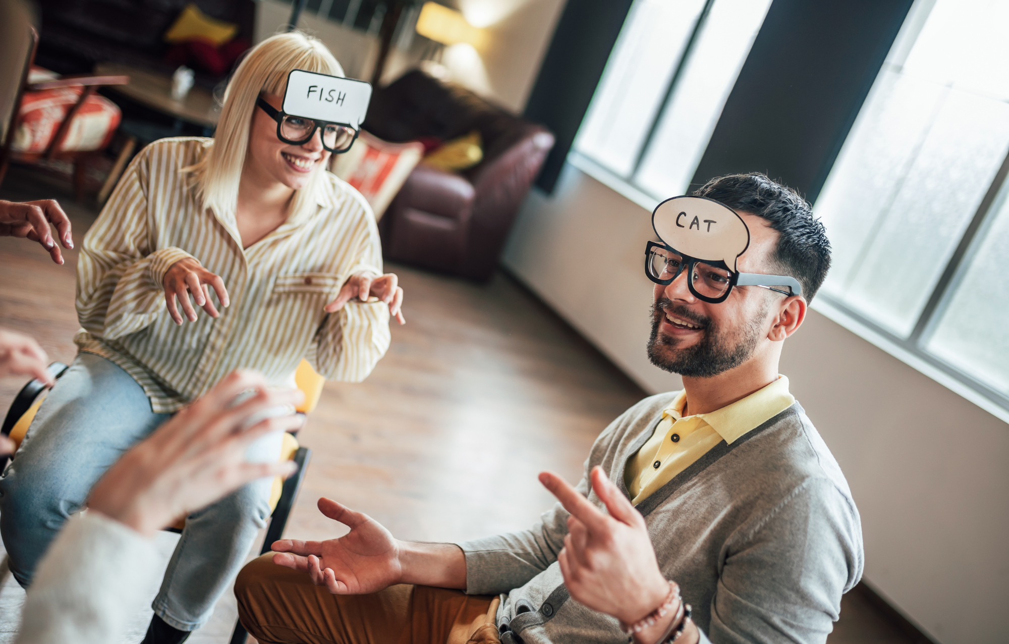 People playing a guessing game where they hold up signs with words like 'FISH' and 'CAT' in a bright, cozy living room.