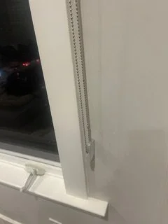 Close-up of a white door frame with a vertical metal chain hanging down, near a window with night view outside.