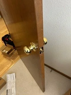 A wooden door slightly ajar with golden doorknobs, leading to a room with a wooden floor and a staircase.