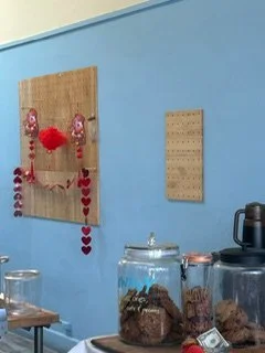 Decorative wall hanging with red hearts and a red pom-pom on a light blue wall.