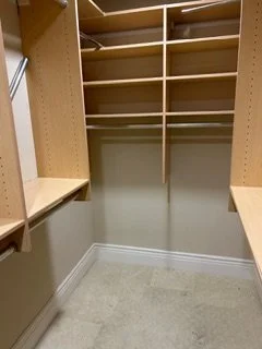Empty walk-in closet with beige built-in shelves and cubbies, beige carpeting, and a white wall.