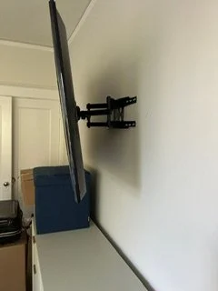 Wall-mounted adjustable TV bracket with a television attached, in a room with white walls and cupboards.