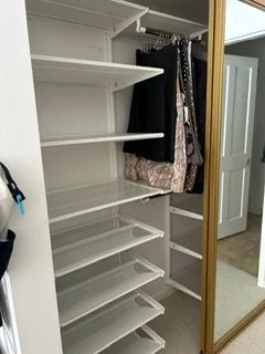 Empty closet with white shelves, hanging clothes, and a mirror on the door.