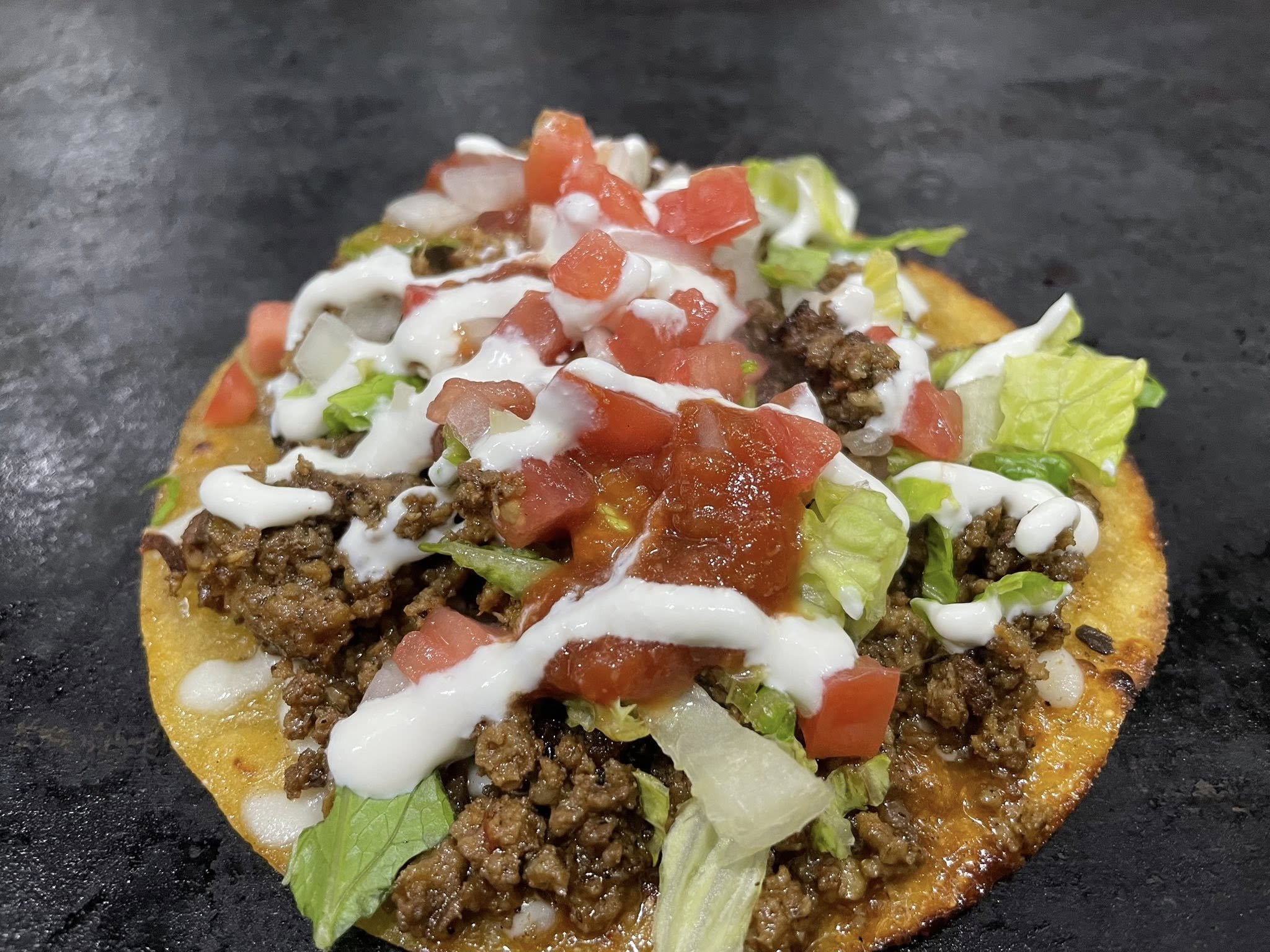 Mini taco with ground beef, shredded lettuce, diced tomatoes, sour cream, and salsa on a corn tortilla