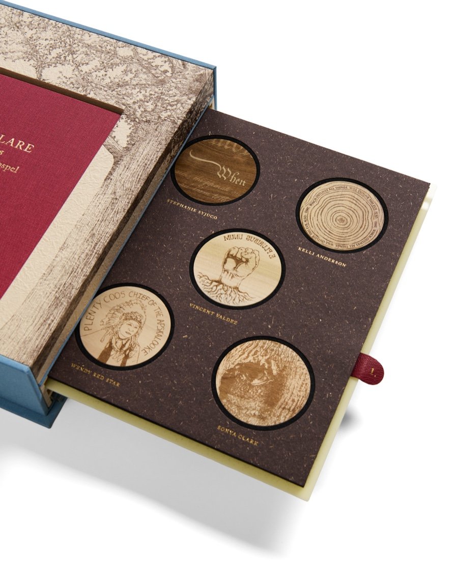 Open box containing a collection of five wooden tokens with engraved illustrations and names, placed on a dark patterned background with a faint, sparkly effect.