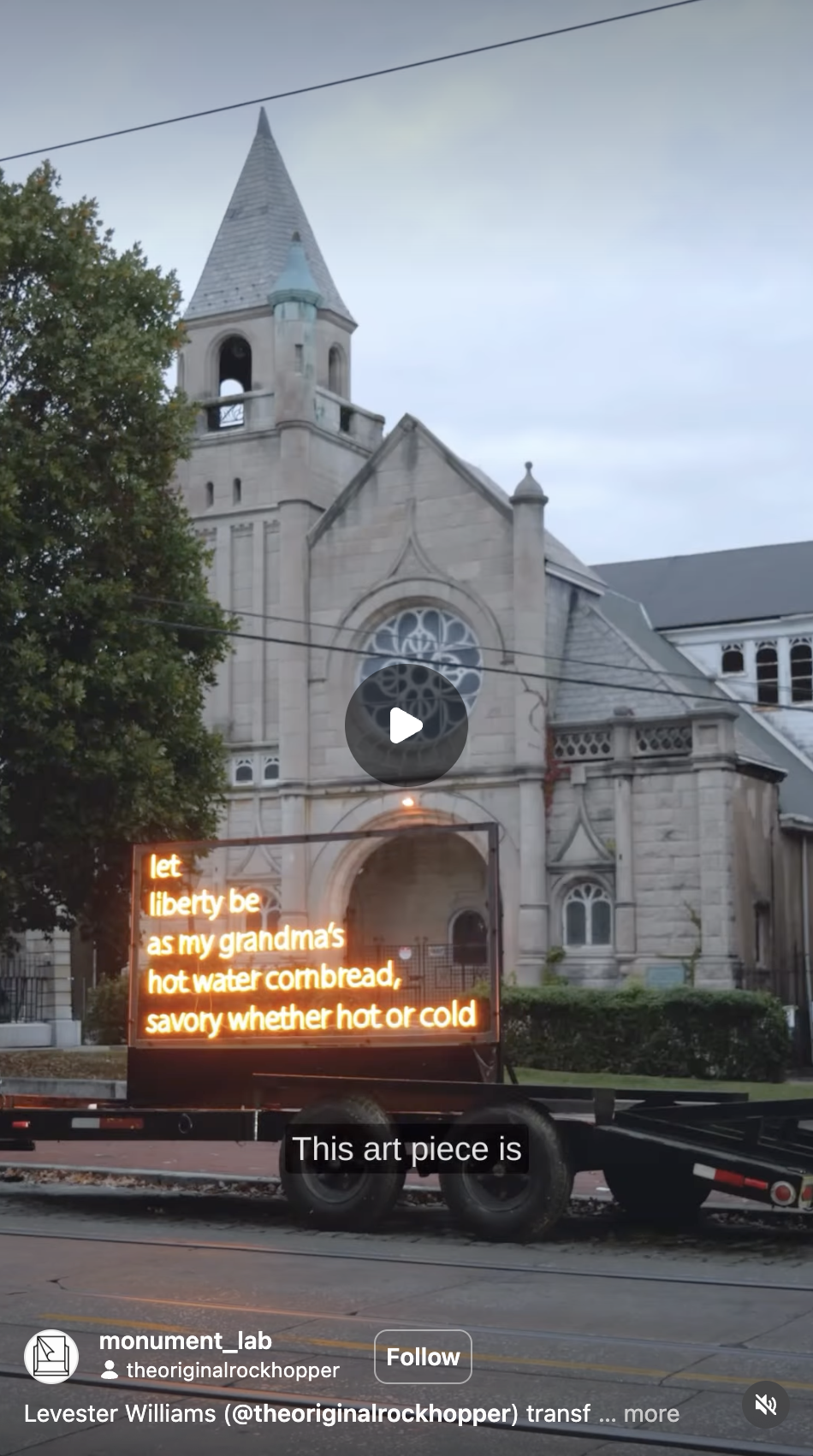 A historic stone church with a tall steeple and a large circular stained glass window. There is a glowing orange neon sign on a small trailer in front of the church displaying text about a grandmother's hot water cornbread.