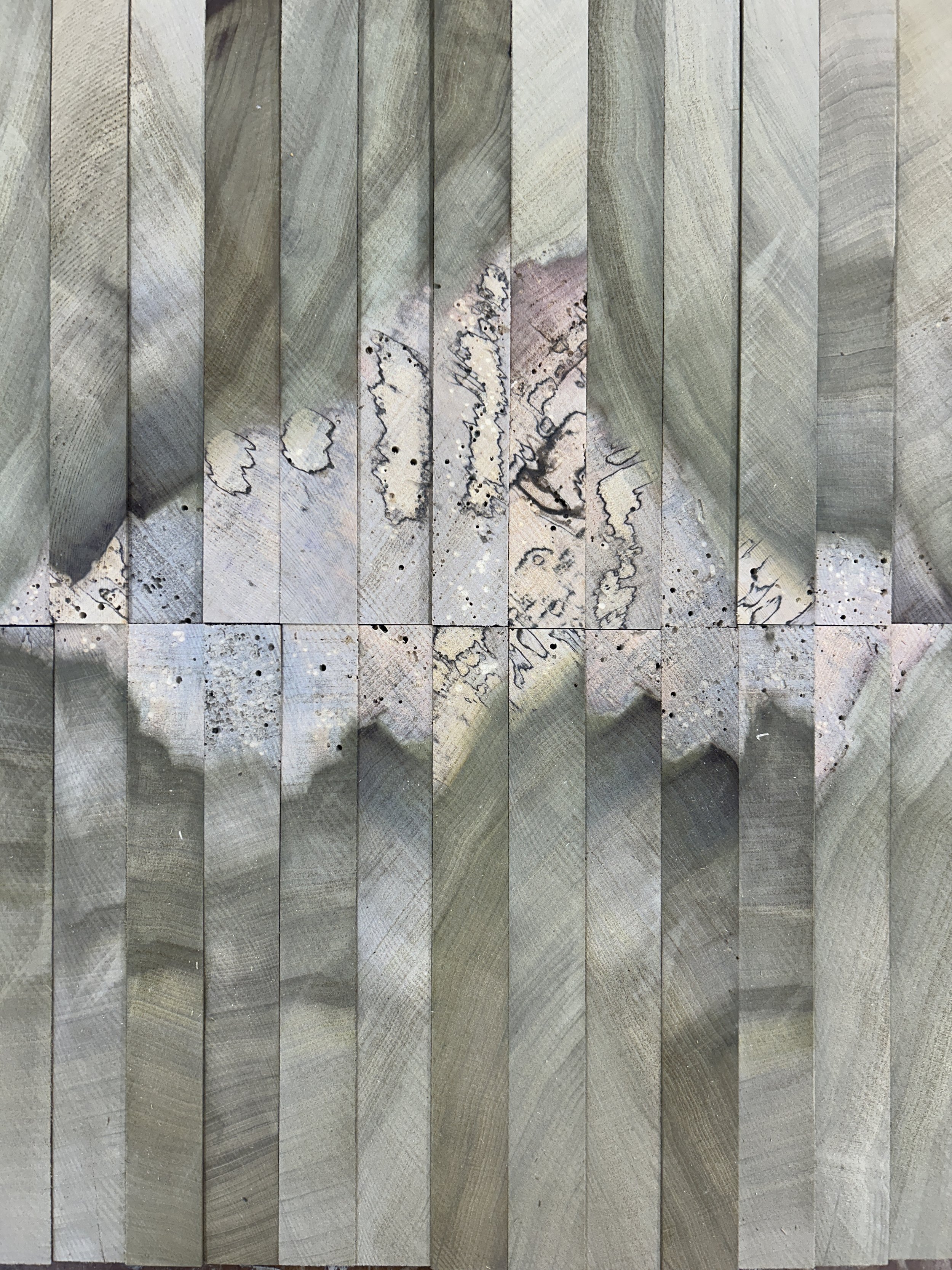Close-up photograph of a textured surface made up of vertical wooden planks with natural wood grain patterns and some black stains or markings.