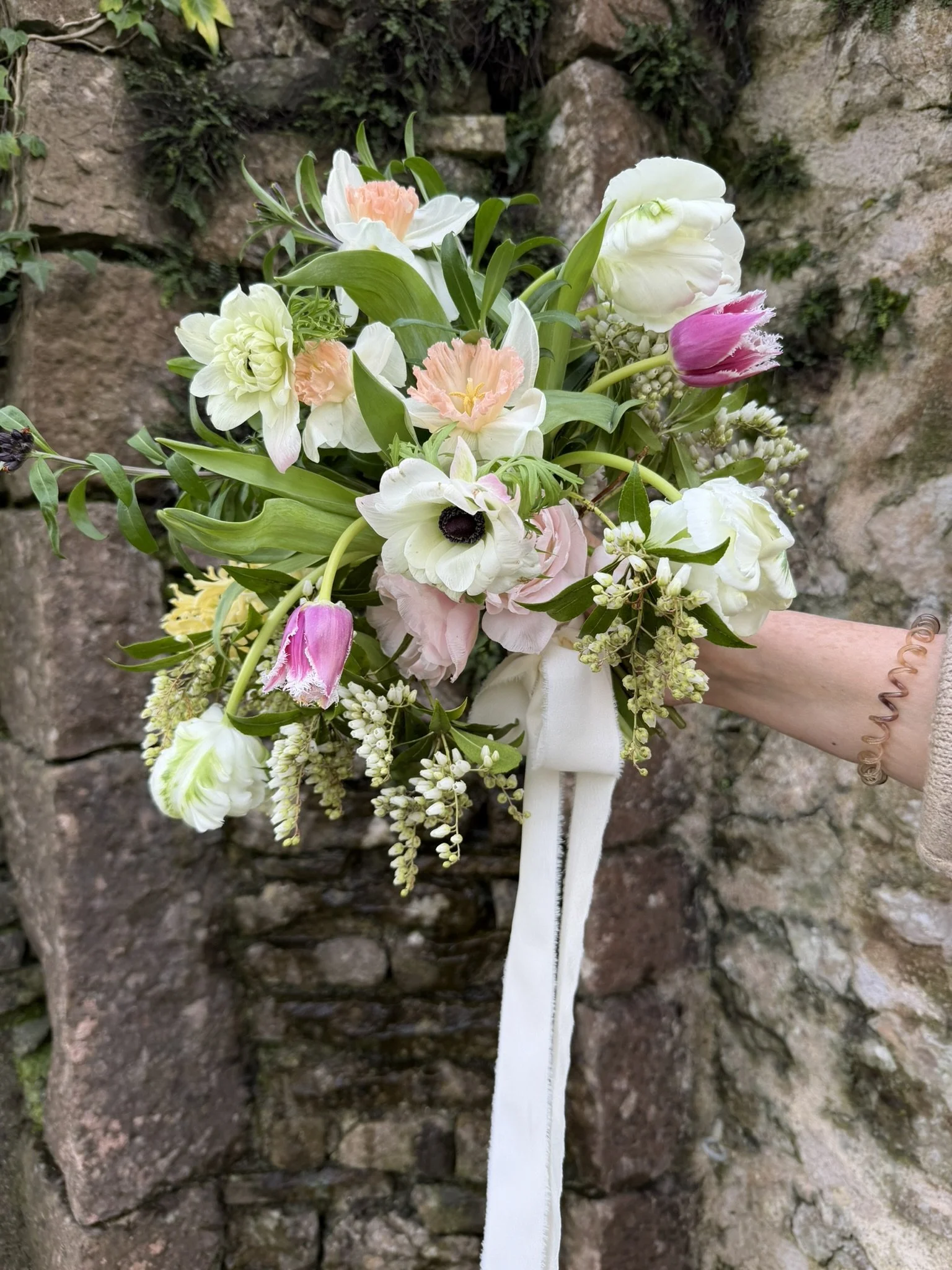 A Spring bridal bouquet. Delicate, soft tulips, daffodils and ranunculus handtied with ribbon. Beautiful bridal bouquets for your wedding in Shropshire.