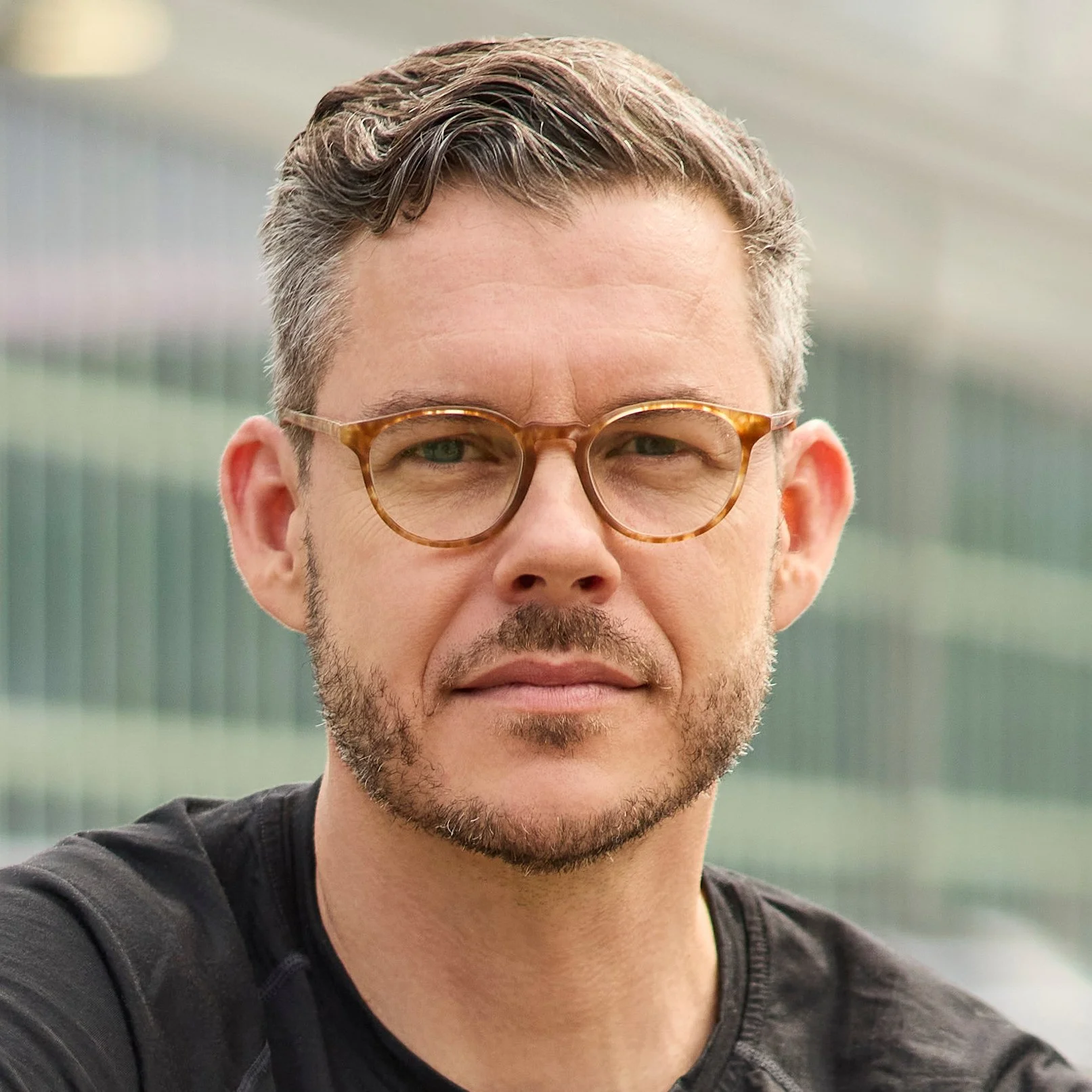 A man with glasses and facial hair, looking directly at the camera with a neutral expression.