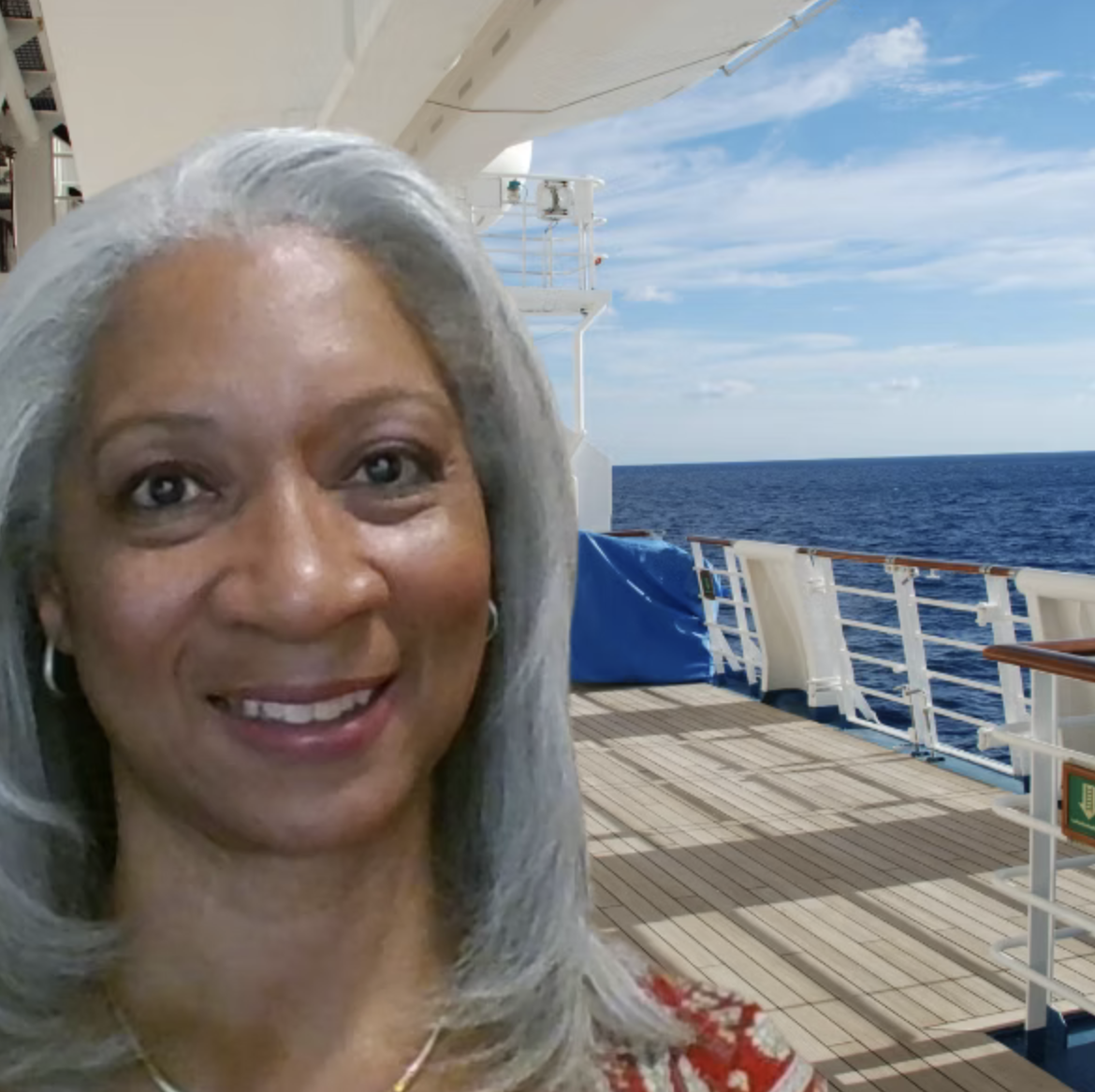 Smiling woman with gray hair taking a selfie on a cruise ship deck with the ocean and blue sky in the background.
